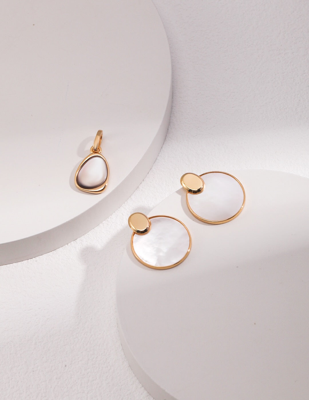 A pair of elegant Minimalist Detachable Mother-Of-Pearl Earrings featuring gold vermeil accents, displayed on a soft fabric background.