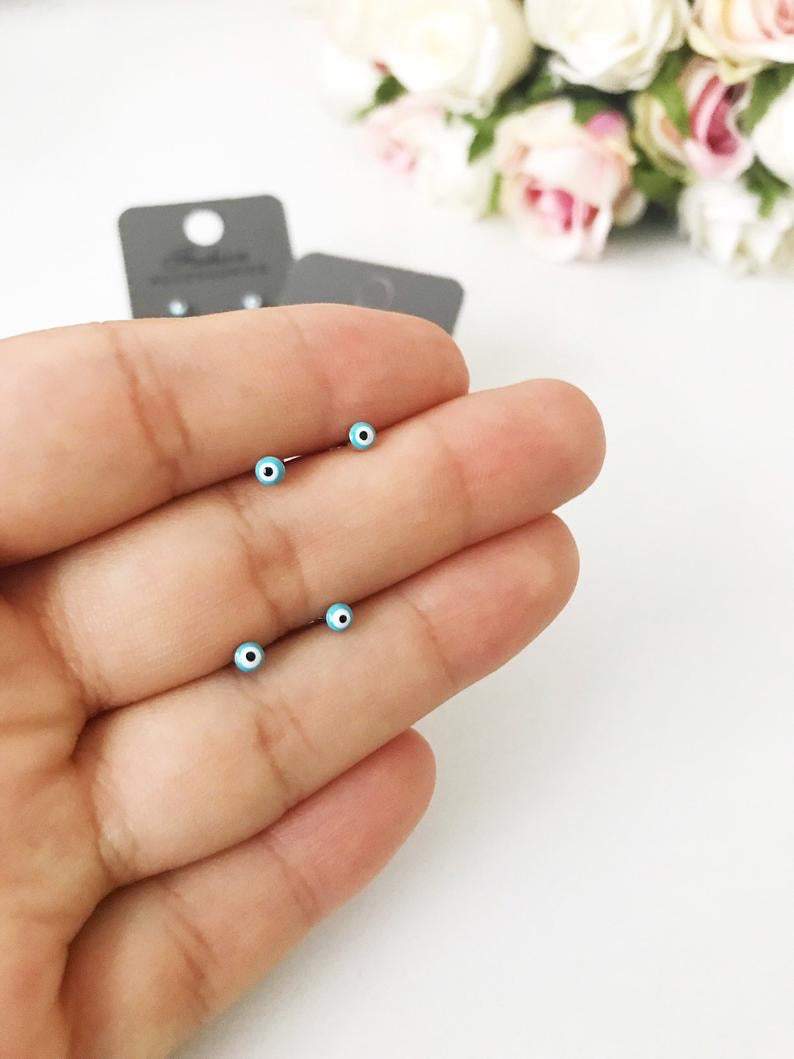 A pair of handmade minimalist evil eye stud earrings with a silver finish, featuring a blue evil eye design, symbolizing protection and good luck.