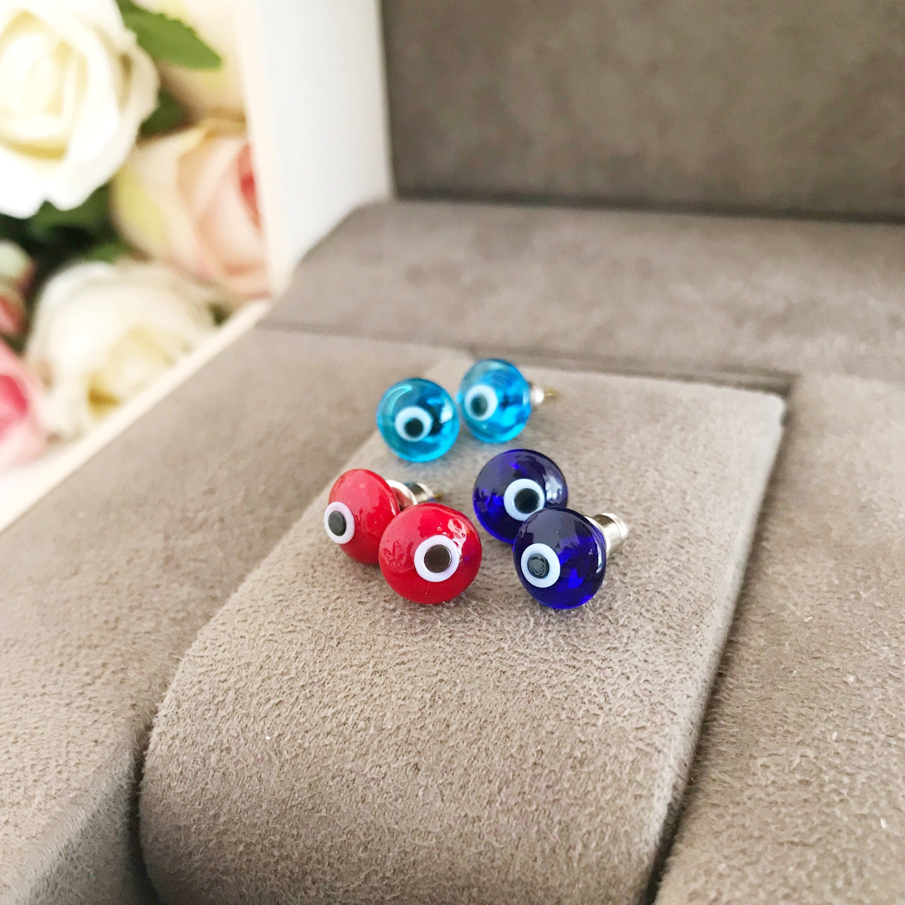 A pair of Minimalist Evil Eye Stud Earrings featuring a silver finish with blue and red evil eye designs, symbolizing protection.