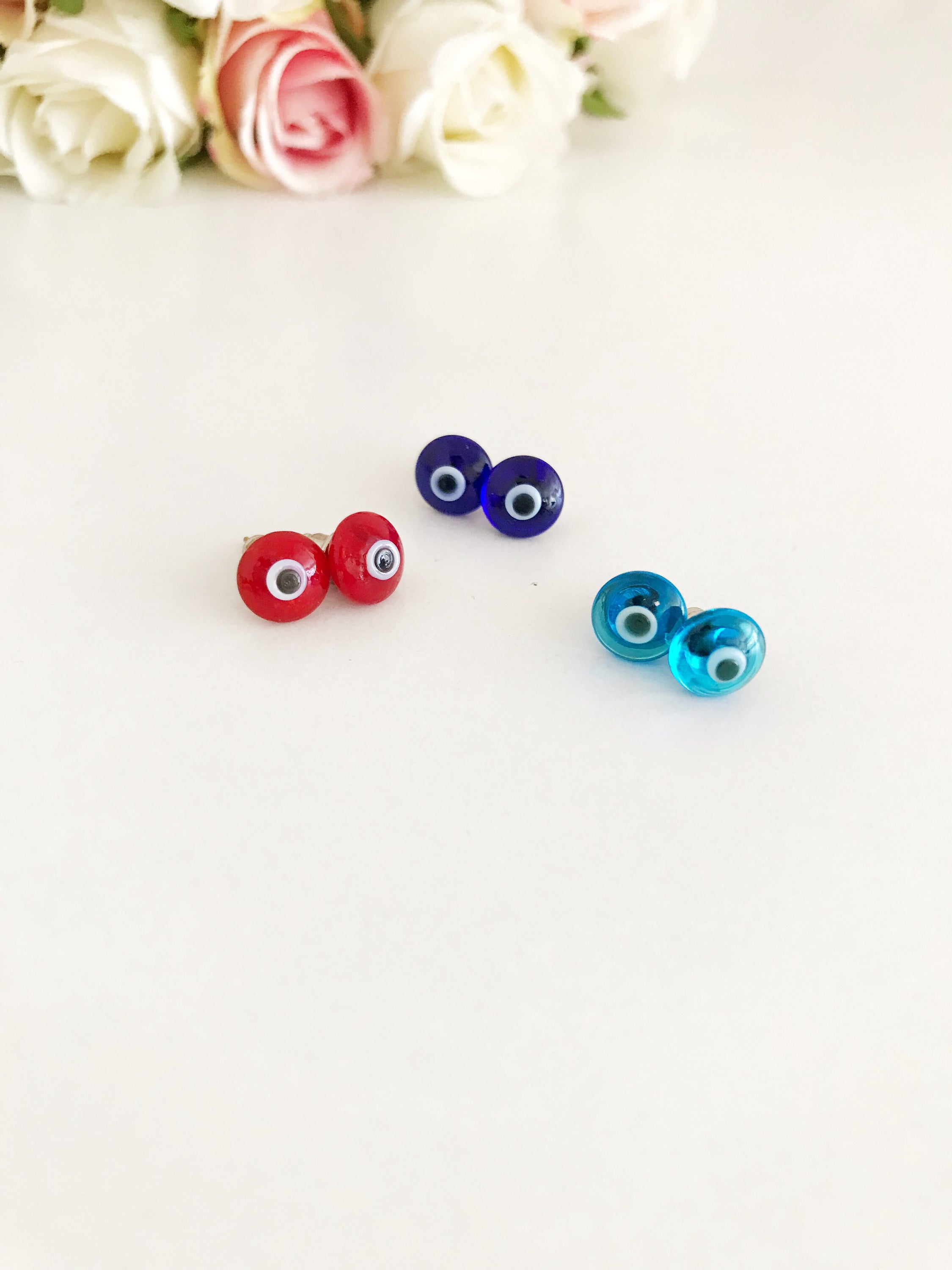 A pair of Minimalist Evil Eye Stud Earrings featuring a silver finish with blue and red evil eye designs, symbolizing protection.