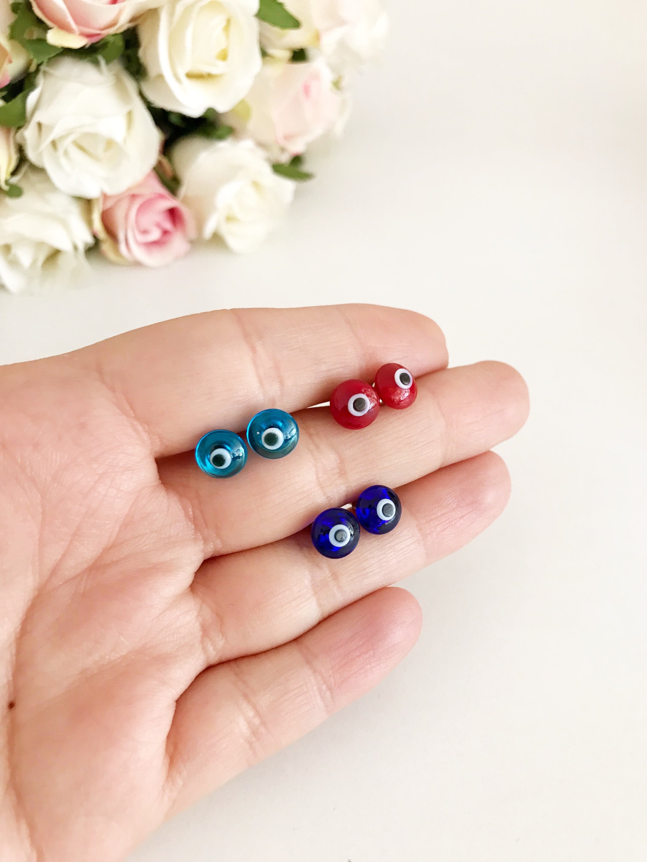 A pair of Minimalist Evil Eye Stud Earrings featuring a silver finish with blue and red evil eye designs, symbolizing protection.