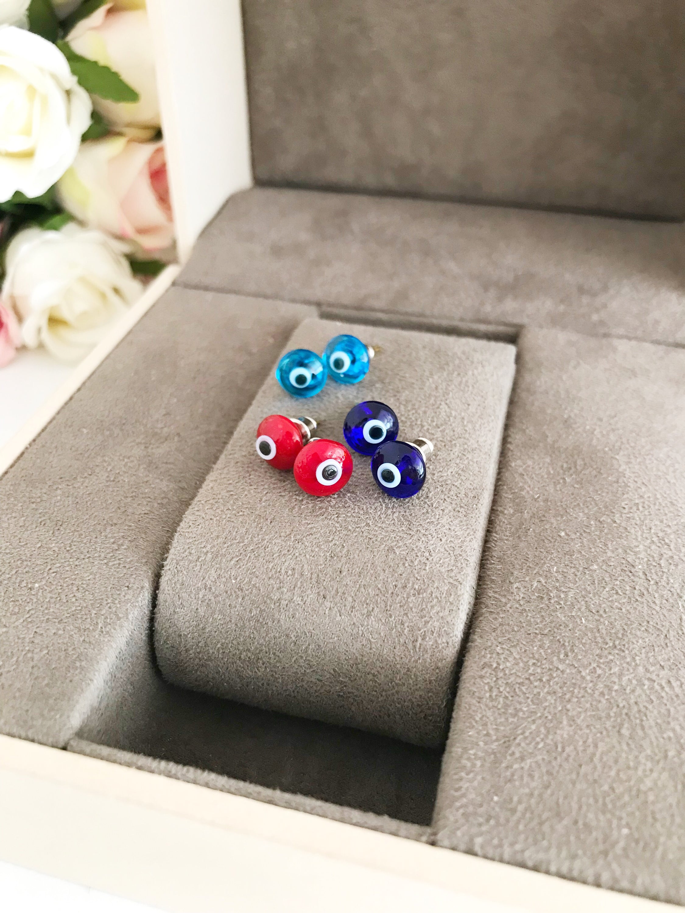 A pair of Minimalist Evil Eye Stud Earrings featuring a silver finish with blue and red evil eye designs, symbolizing protection.