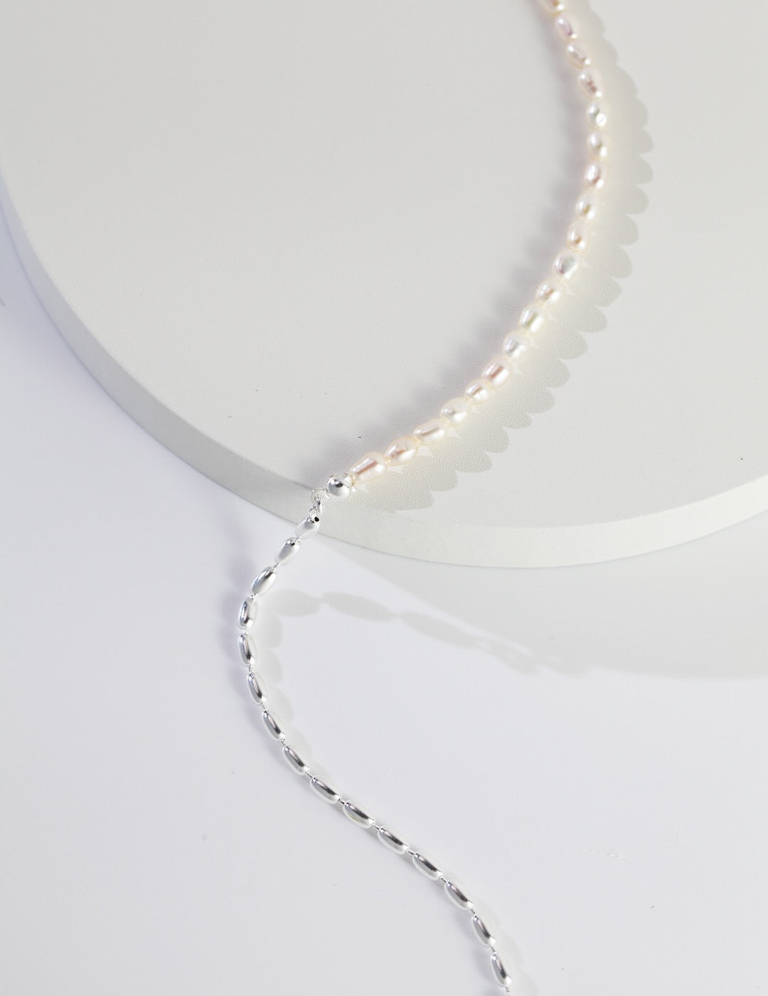 A delicate Minimalist Rice Bead Chain Asymmetric Necklace featuring natural pearls and sterling silver, elegantly displayed on a soft background.