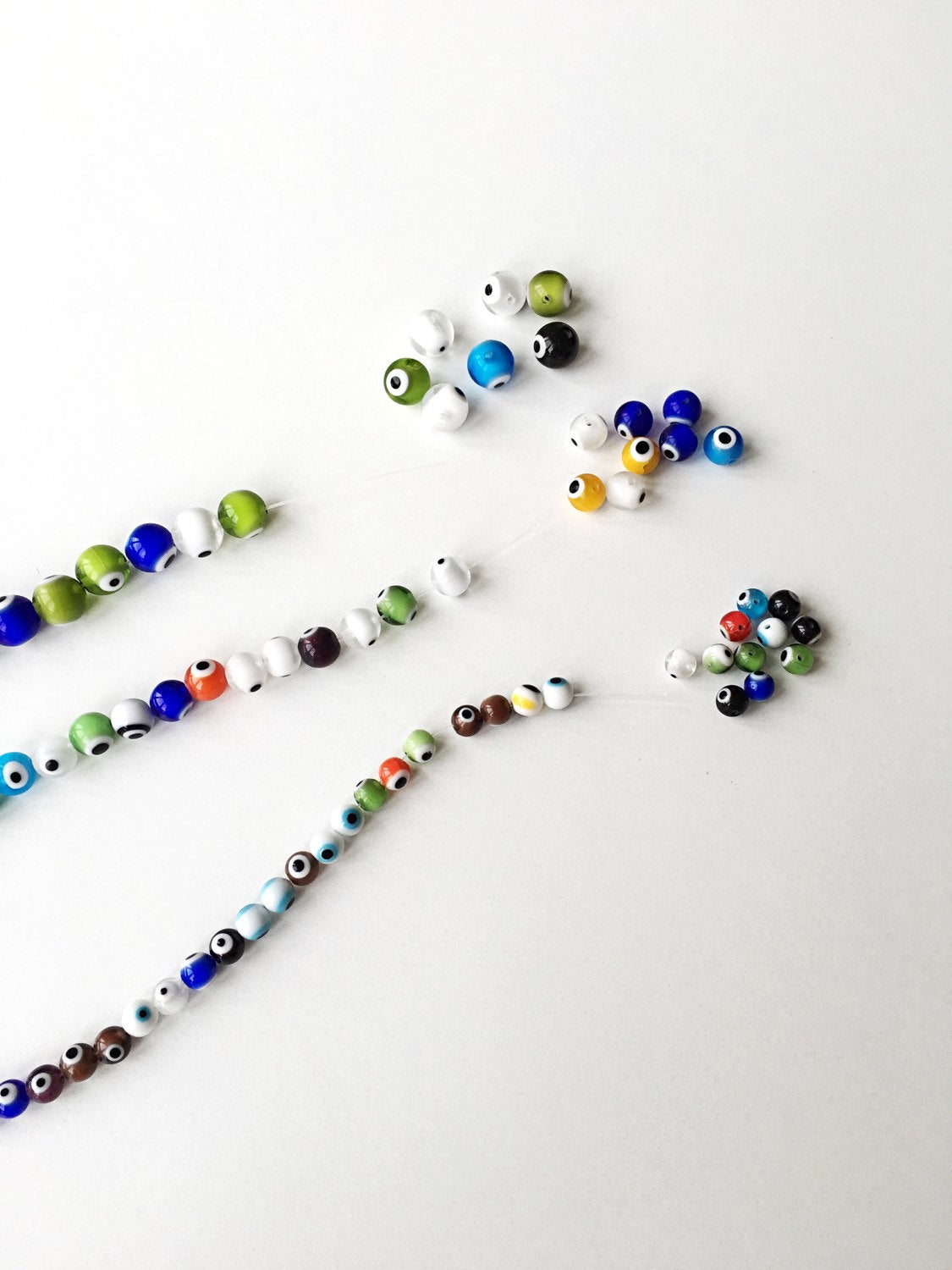 A collection of mixed color evil eye beads in 6mm, 8mm, and 10mm sizes, showcasing their vibrant designs and handmade quality.