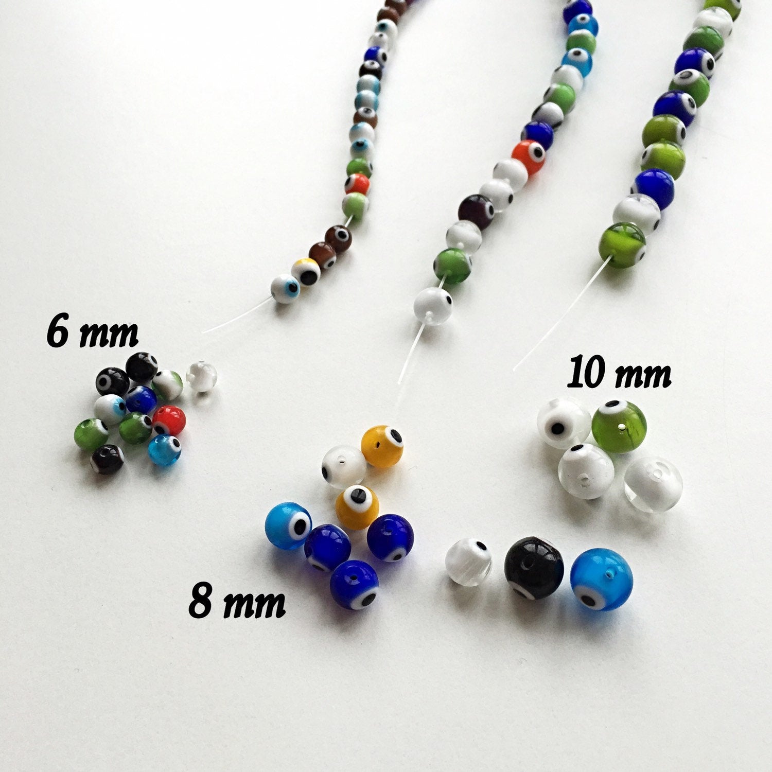 A collection of mixed color evil eye beads in 6mm, 8mm, and 10mm sizes, showcasing their vibrant designs and handmade quality.