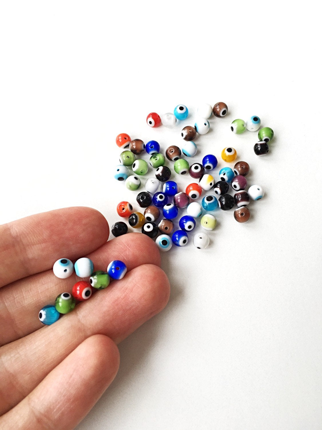 A collection of mixed color evil eye beads in 6mm, 8mm, and 10mm sizes, showcasing their vibrant designs and handmade quality.