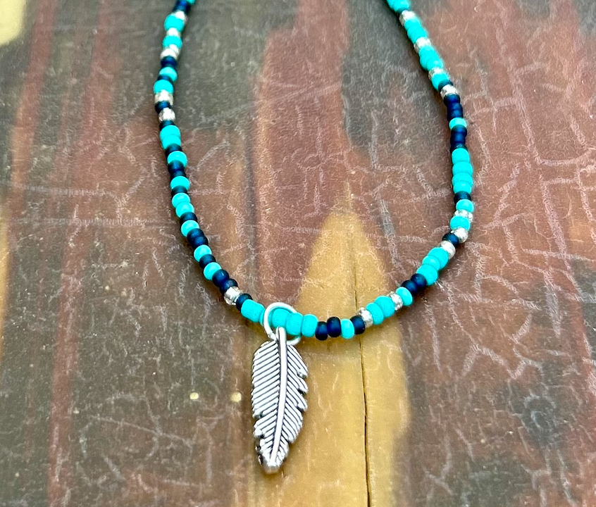 A vibrant Mixed Turquoise Navy Boho Seed Bead Necklace featuring a silver feather pendant, showcasing colorful Czech glass seed beads on elastic cording.