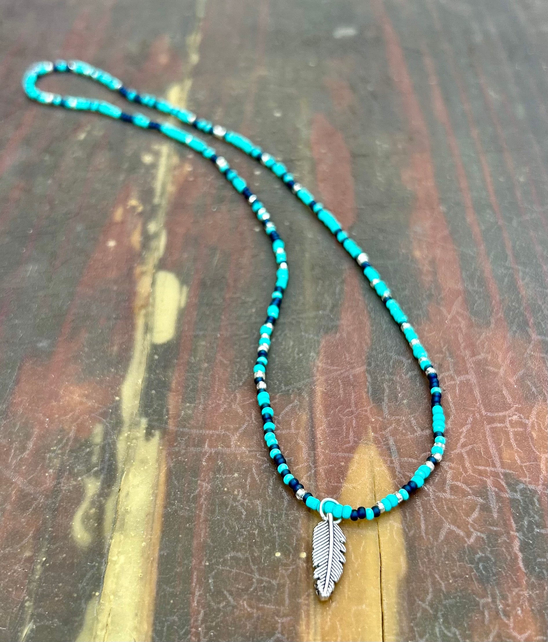 A vibrant Mixed Turquoise Navy Boho Seed Bead Necklace featuring a silver feather pendant, showcasing colorful Czech glass seed beads on elastic cording.