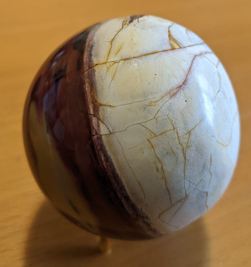 A beautifully crafted Mookaite Jasper Sphere showcasing vibrant colors of red, yellow, purple, and brown, symbolizing emotional growth and connection to nature.