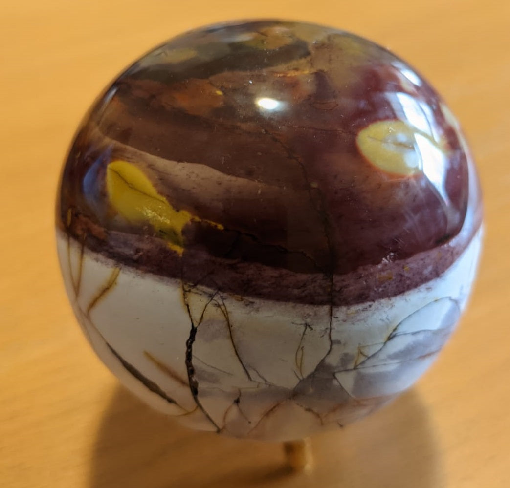 A beautifully crafted Mookaite Jasper Sphere showcasing vibrant colors of red, yellow, purple, and brown, symbolizing emotional growth and connection to nature.