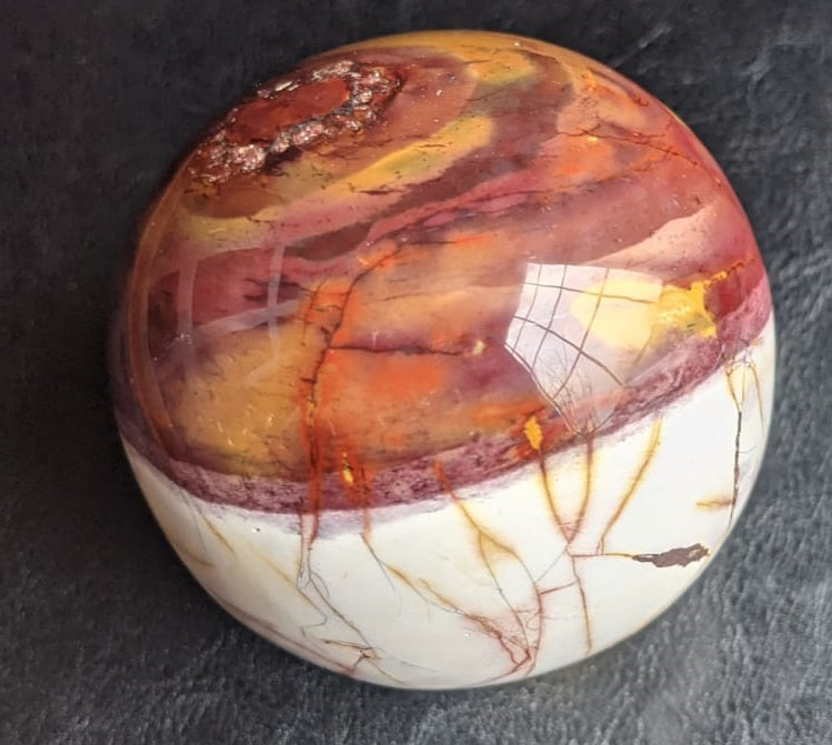 A beautifully crafted Mookaite Jasper Sphere showcasing vibrant colors of red, yellow, purple, and brown, symbolizing emotional growth and connection to nature.