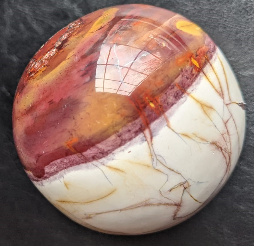 A beautifully crafted Mookaite Jasper Sphere showcasing vibrant colors of red, yellow, purple, and brown, symbolizing emotional growth and connection to nature.