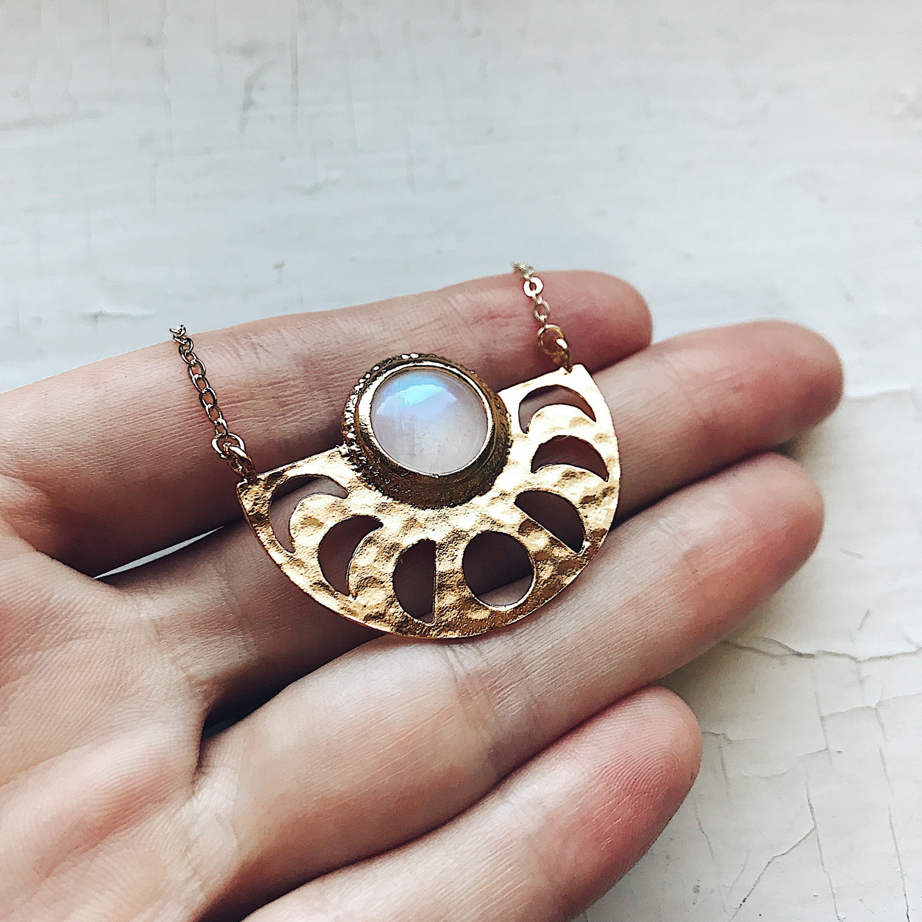 Moon Goddess Necklace featuring a gold tone raw brass pendant with phases of the Moon and a rainbow Moonstone centerpiece.