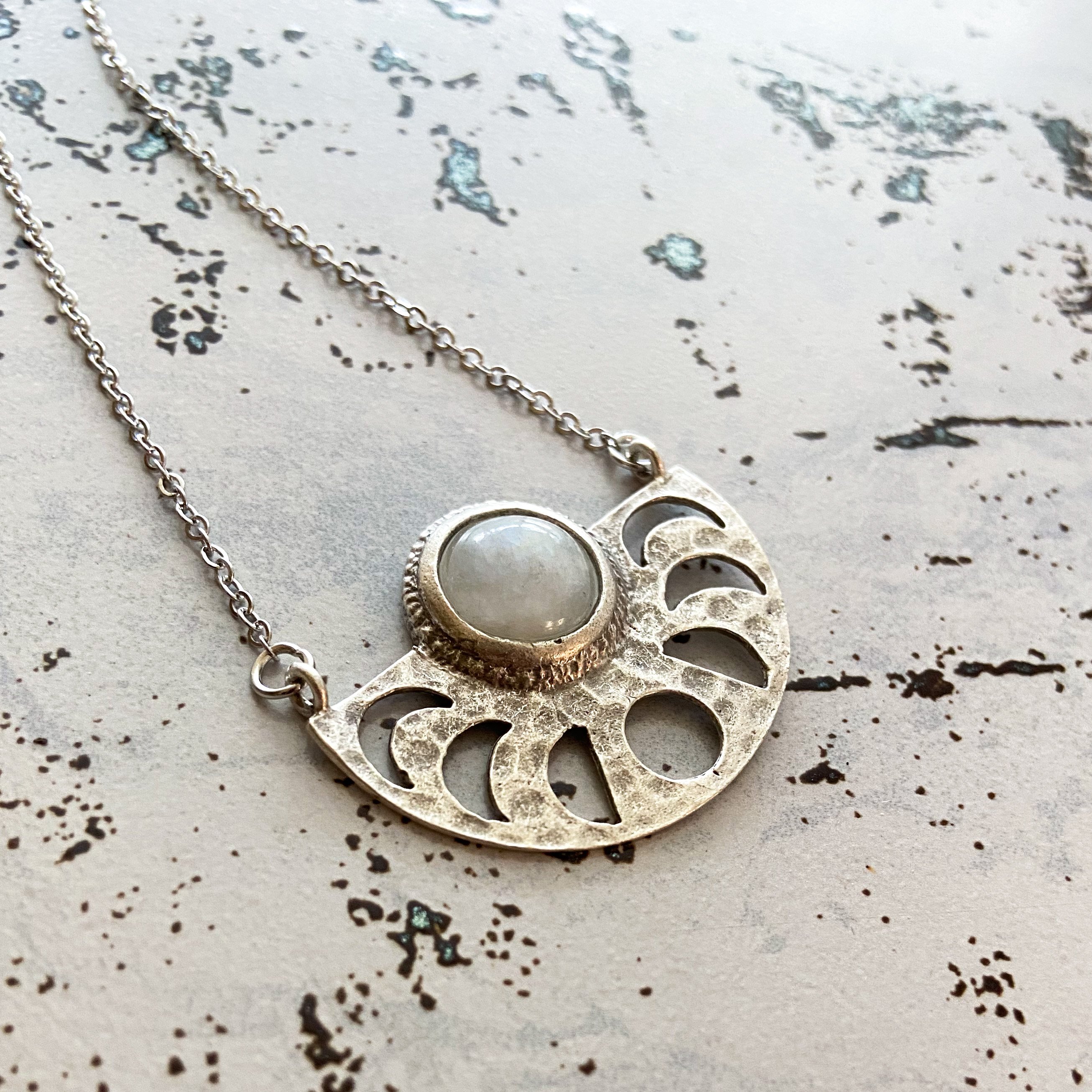 Moon Goddess Necklace featuring a gold tone raw brass pendant with phases of the Moon and a rainbow Moonstone centerpiece.