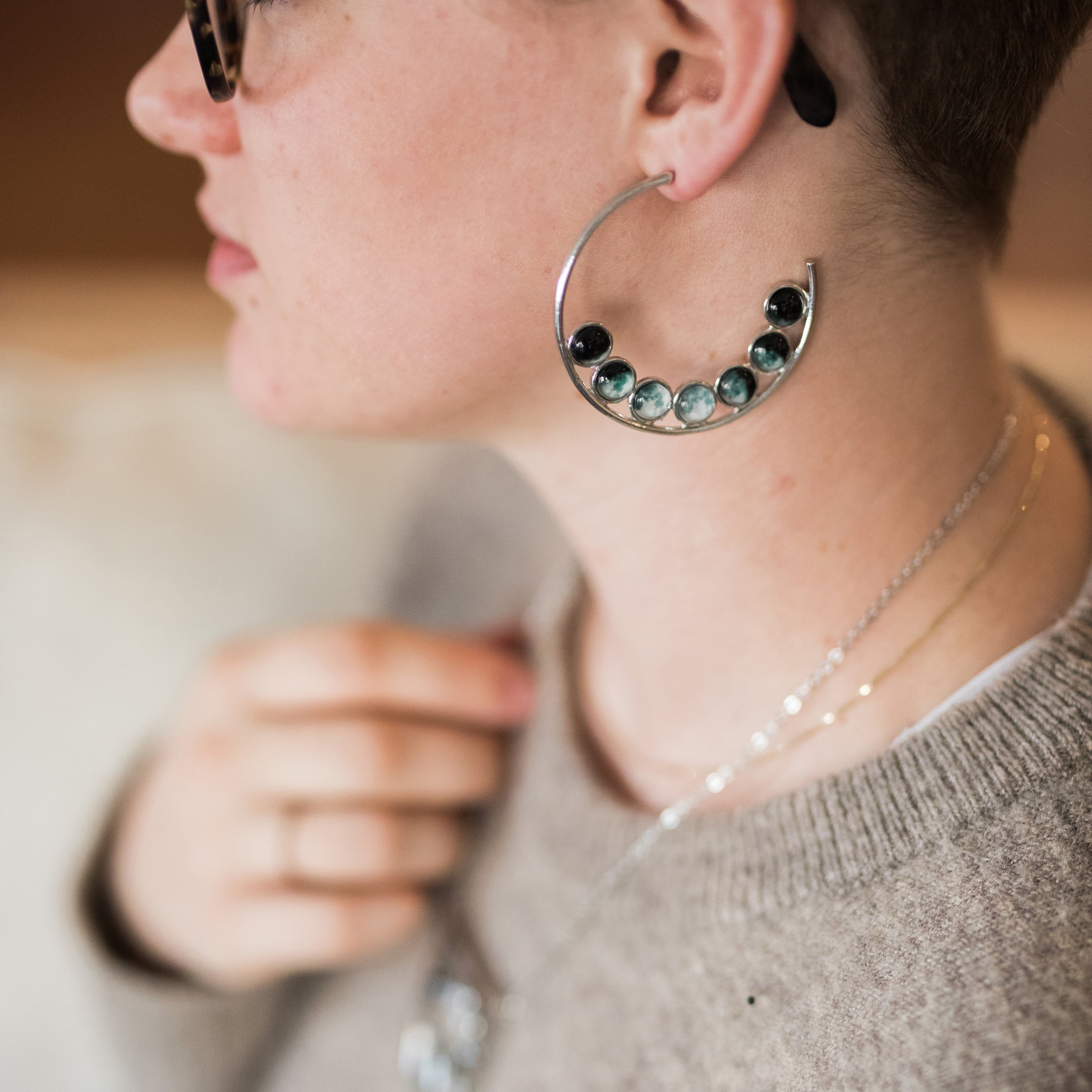 A pair of silver-tone hoop earrings featuring seven phases of the Moon, handcrafted with a textured metal back.