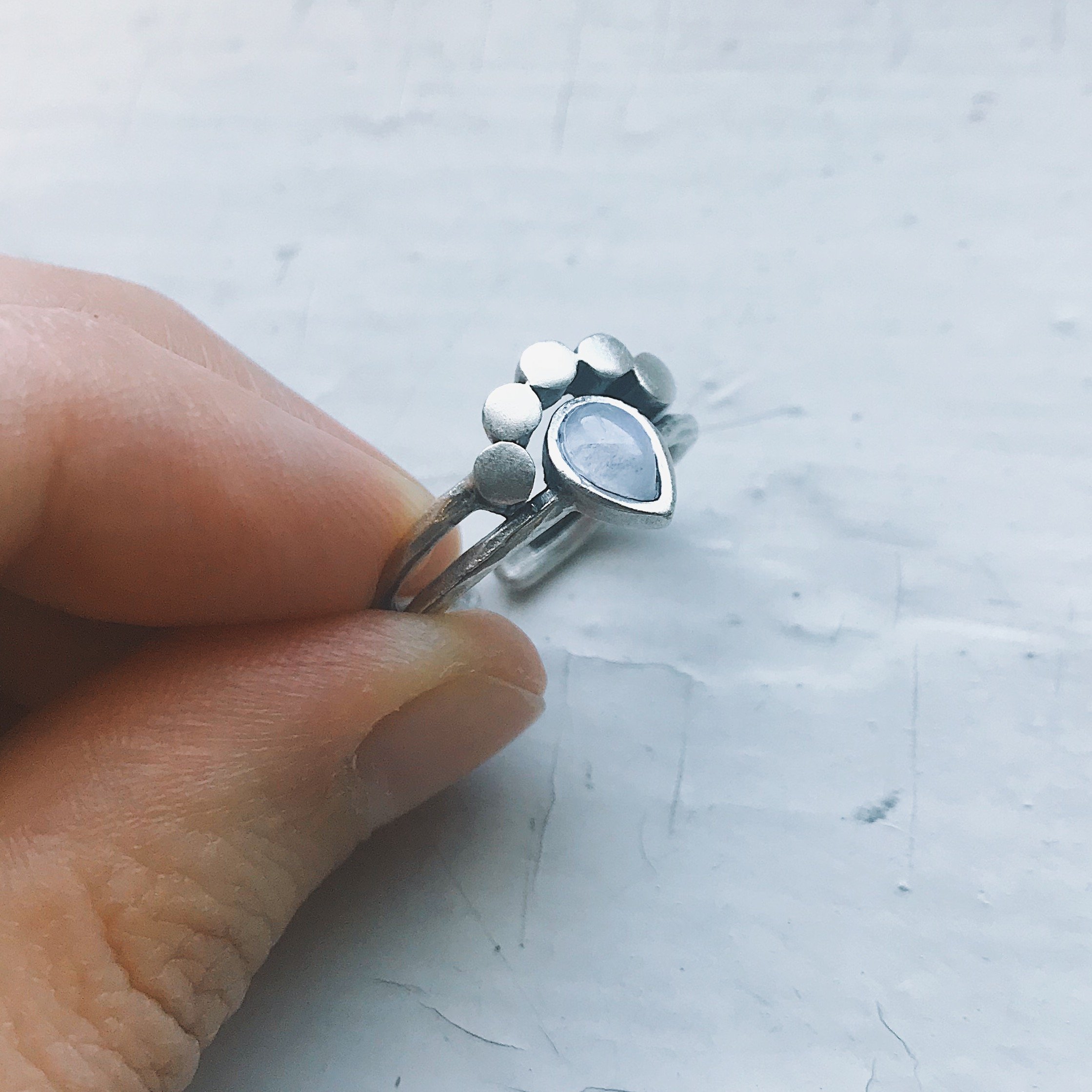 Moondrop Moonstone Ring featuring a teardrop rainbow Moonstone in a bezel surrounded by beads, available in silver and gold tone.