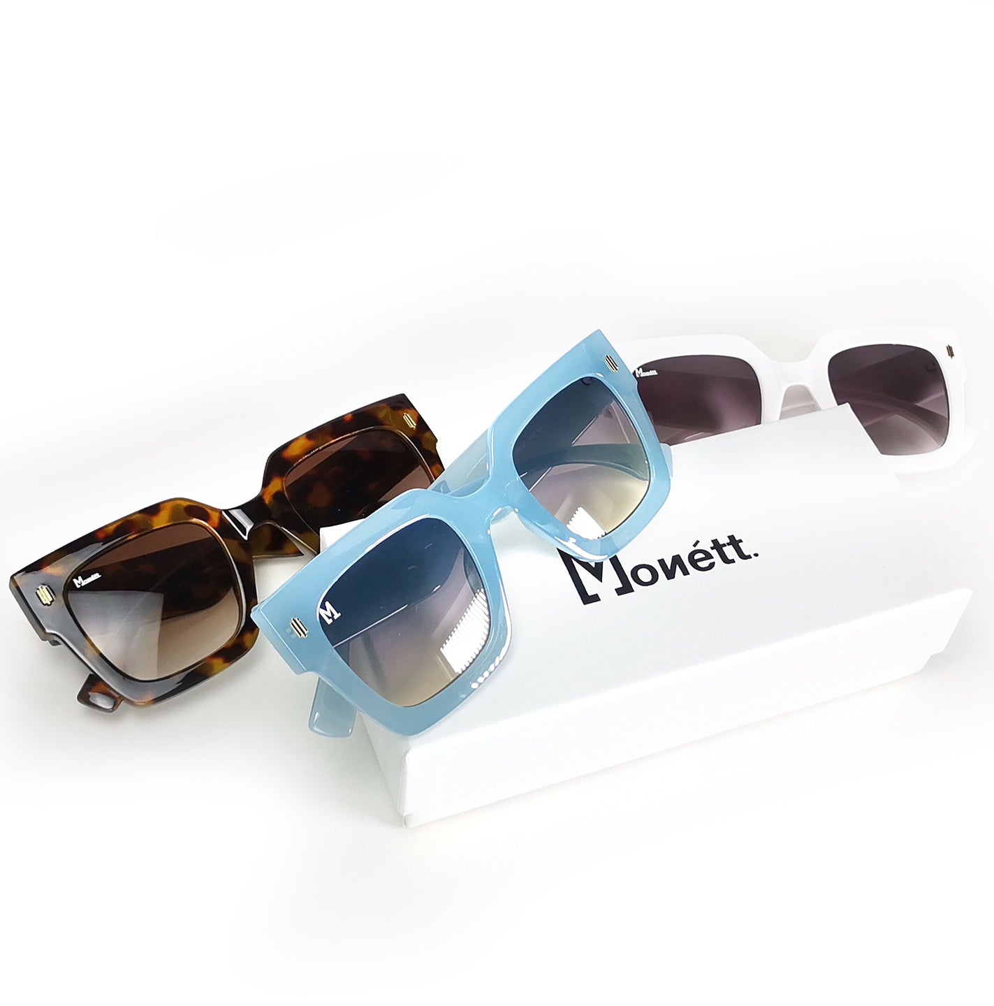 Monett Estilo sunglasses featuring a stylish square frame in minty blue, white, and brown colors, with a cleaning cloth and carry purse.