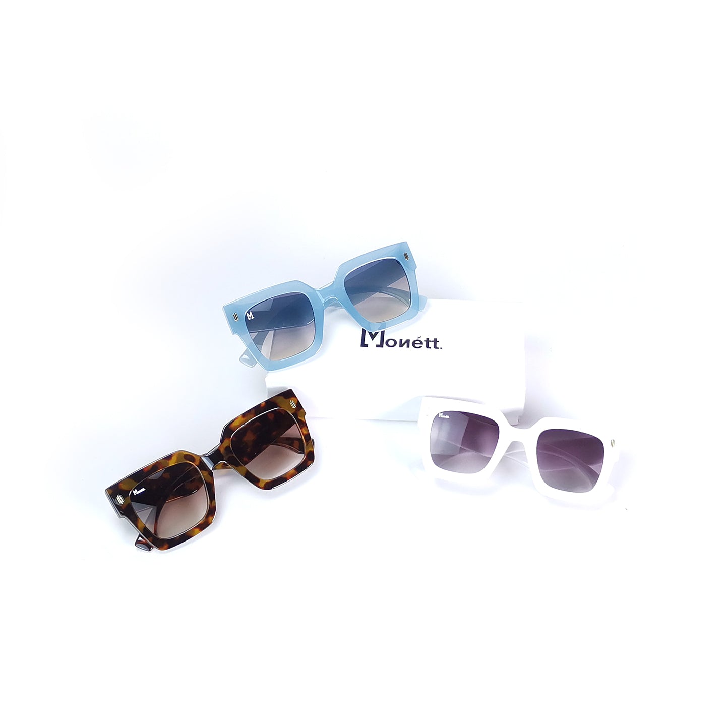 Monett Estilo sunglasses featuring a stylish square frame in minty blue, white, and brown colors, with a cleaning cloth and carry purse.