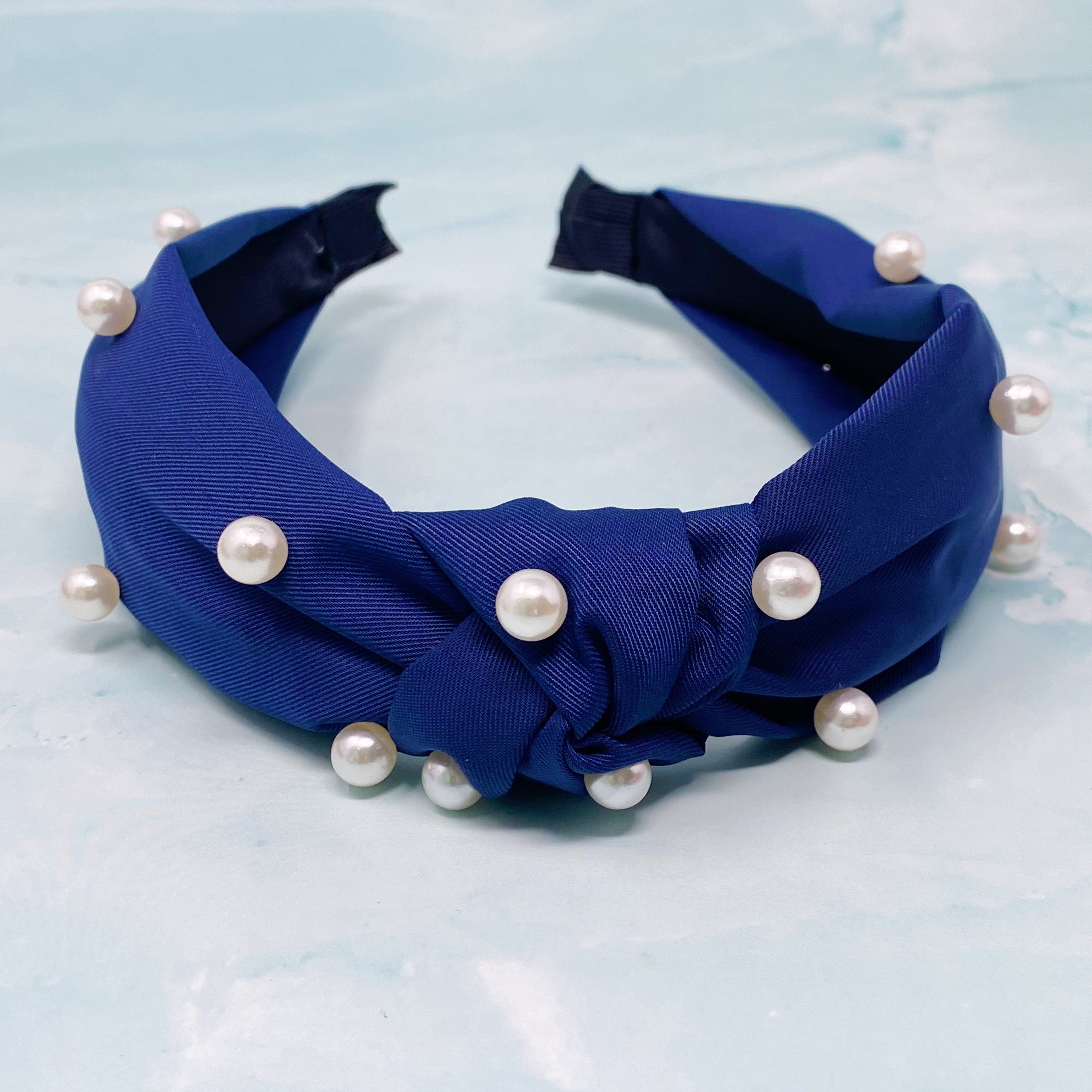 A stylish knotted headband adorned with pearls, perfect for enhancing any outfit.