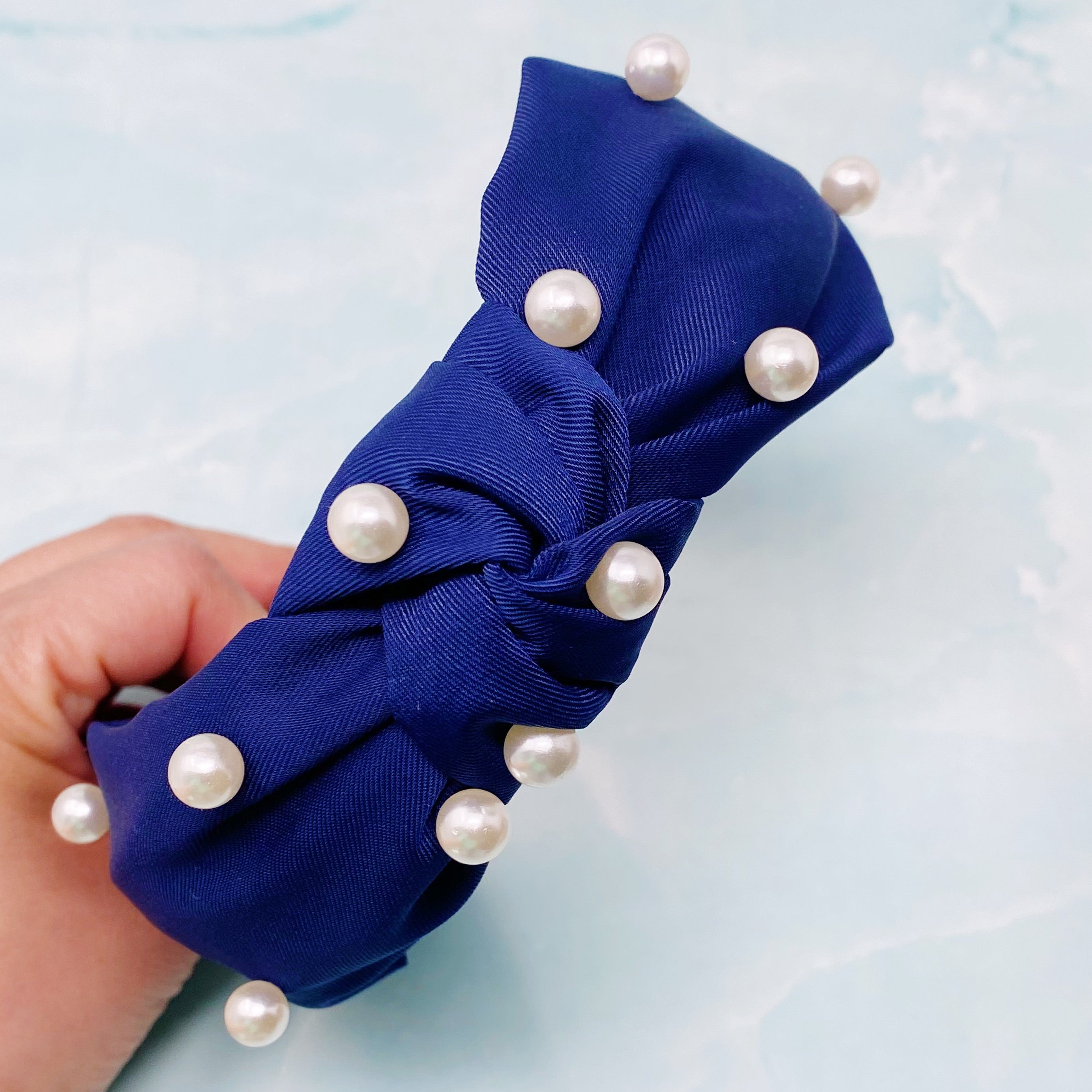 A stylish knotted headband adorned with pearls, perfect for enhancing any outfit.