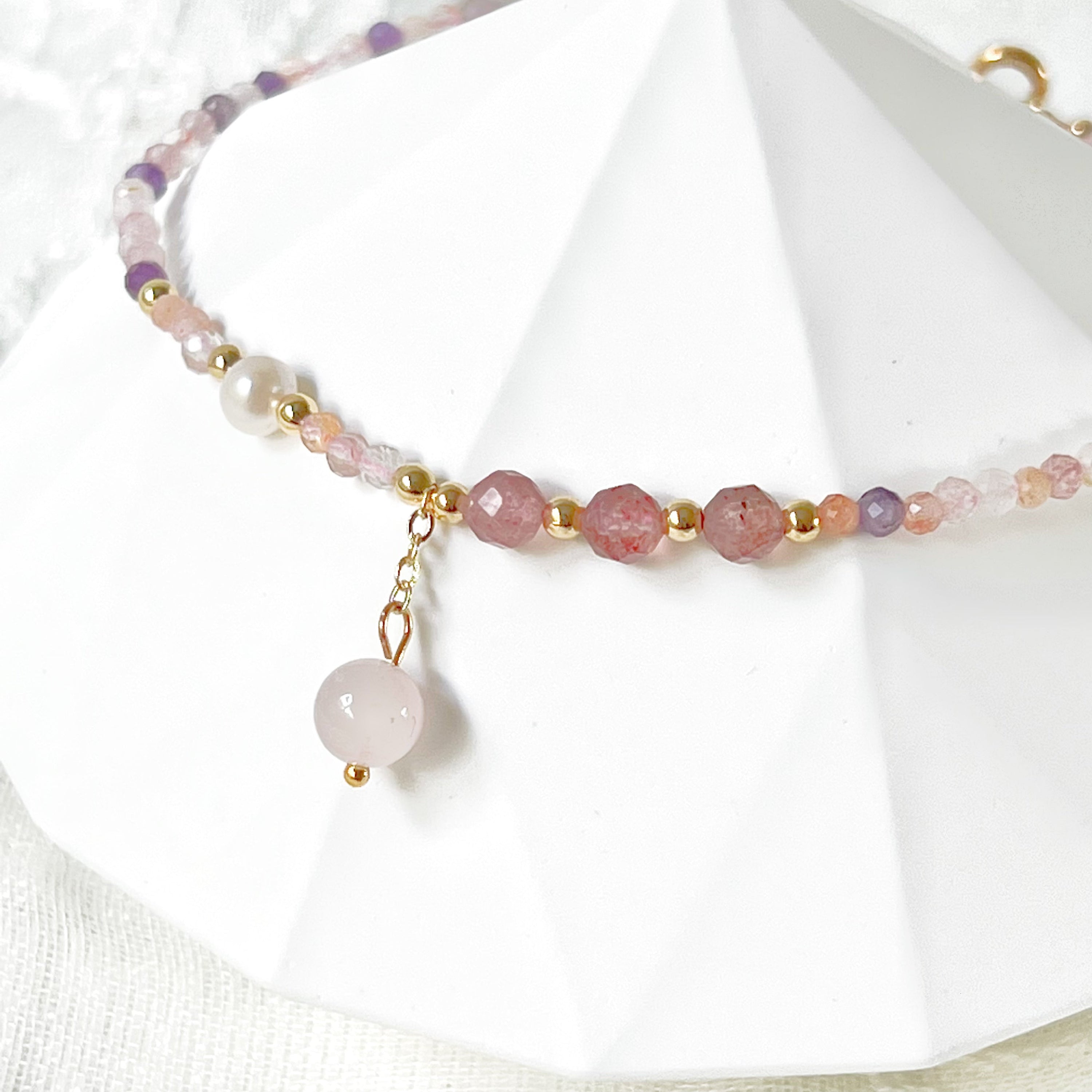 Natural rose quartz and amethyst beaded ankle bracelet with gold-tone accents, showcasing unique crystal patterns.