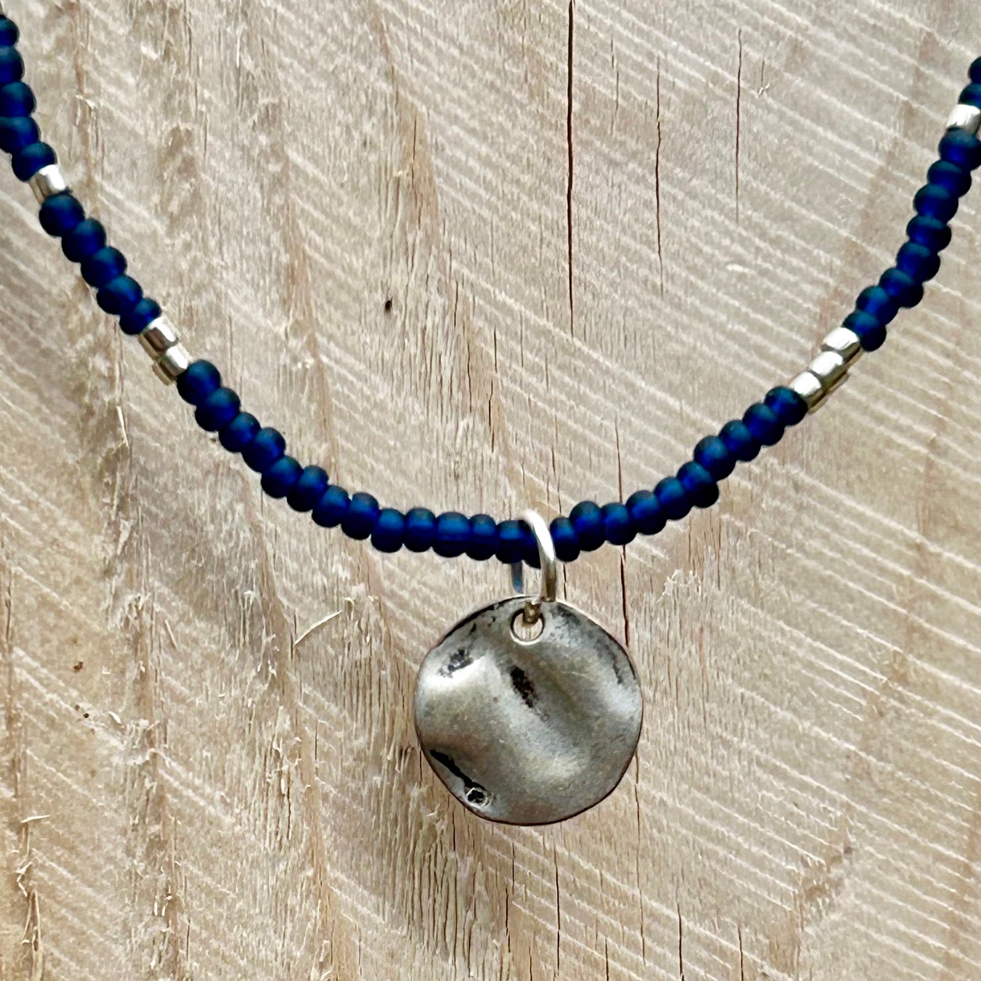 Navy blue boho seed bead necklace featuring silver and coin charm, elegantly displayed on a neutral background.