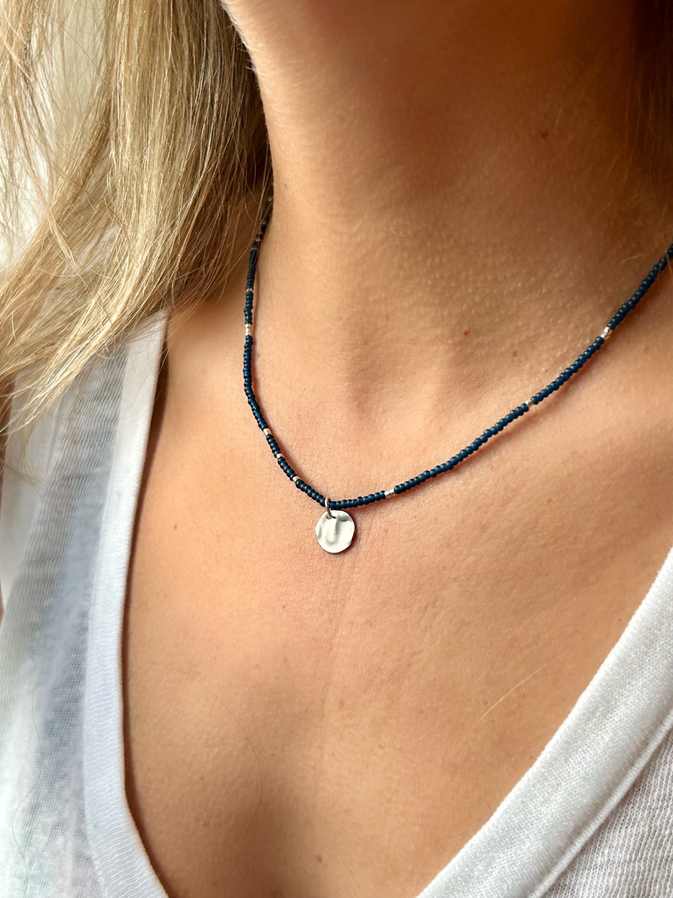 Navy blue boho seed bead necklace featuring silver and coin charm, elegantly displayed on a neutral background.