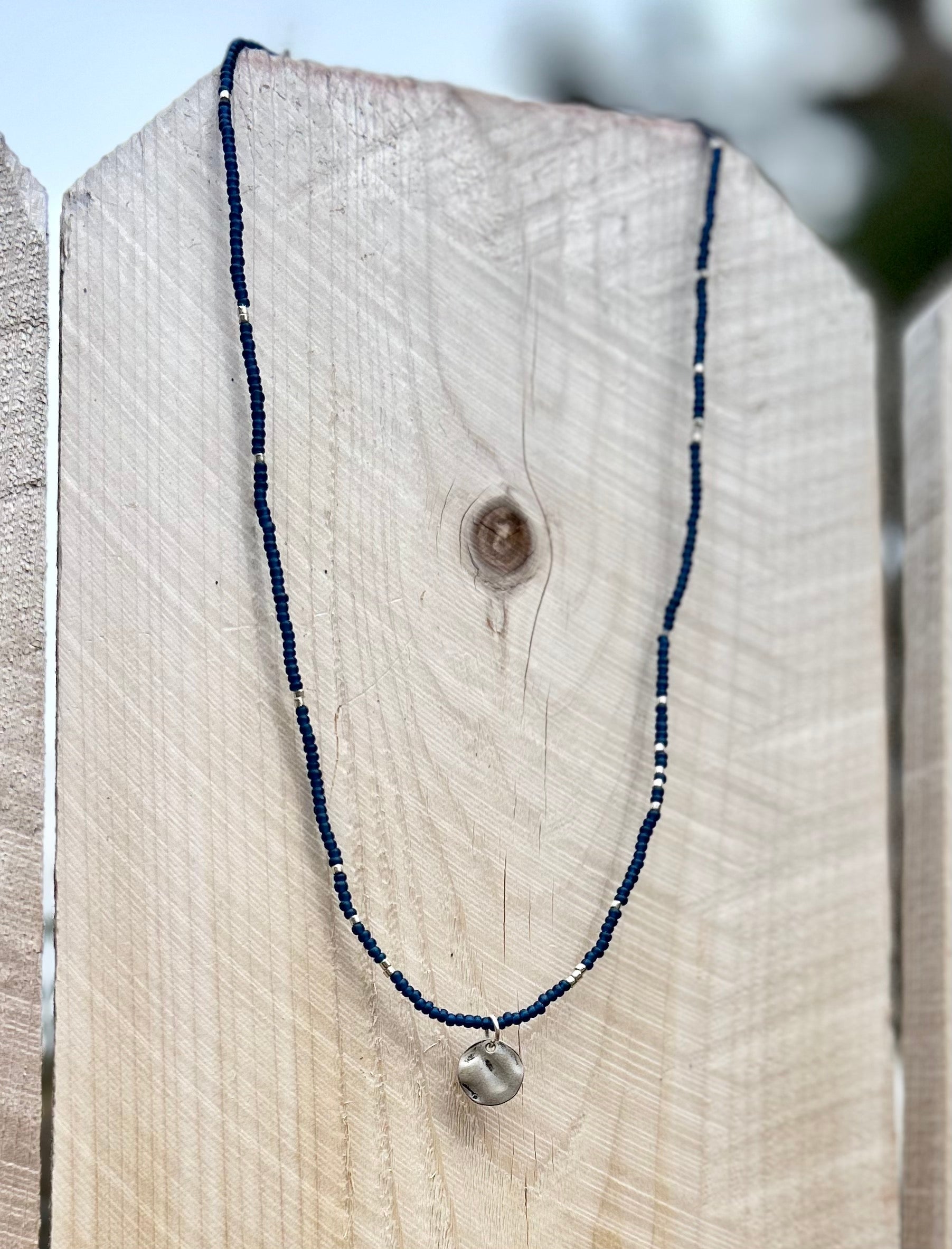 Navy blue boho seed bead necklace featuring silver and coin charm, elegantly displayed on a neutral background.