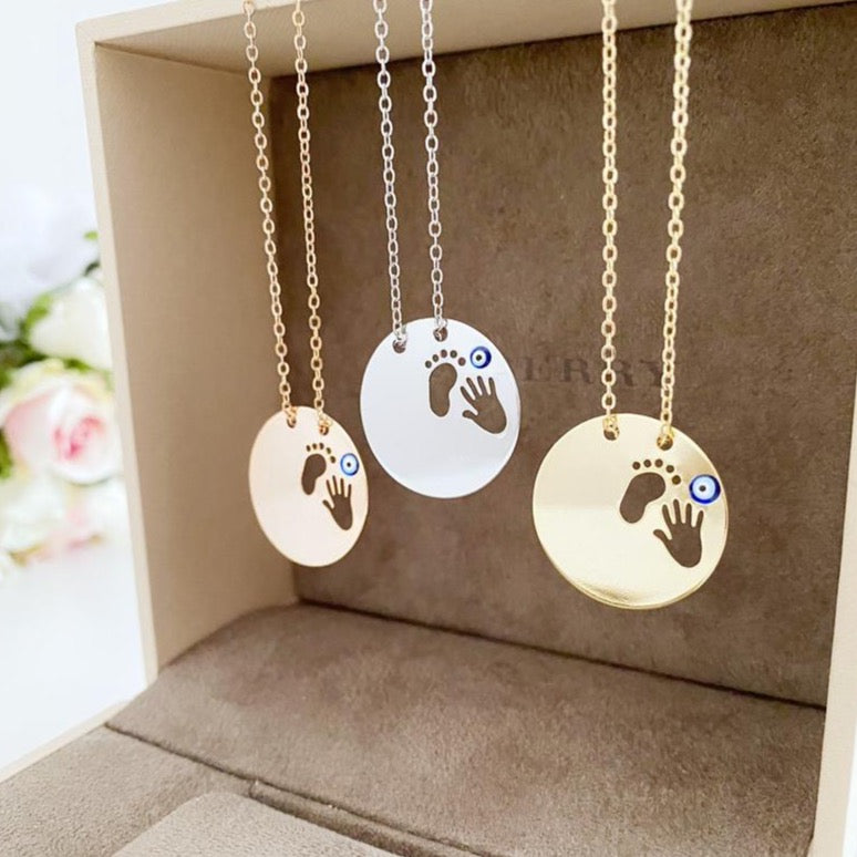 New Baby Necklace featuring an Evil Eye design with baby feet and handprint motifs, available in gold, silver, and rose gold.