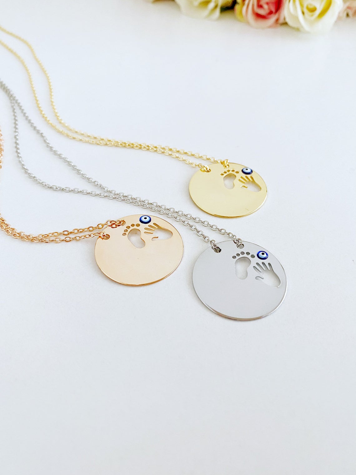 New Baby Necklace featuring an Evil Eye design with baby feet and handprint motifs, available in gold, silver, and rose gold.