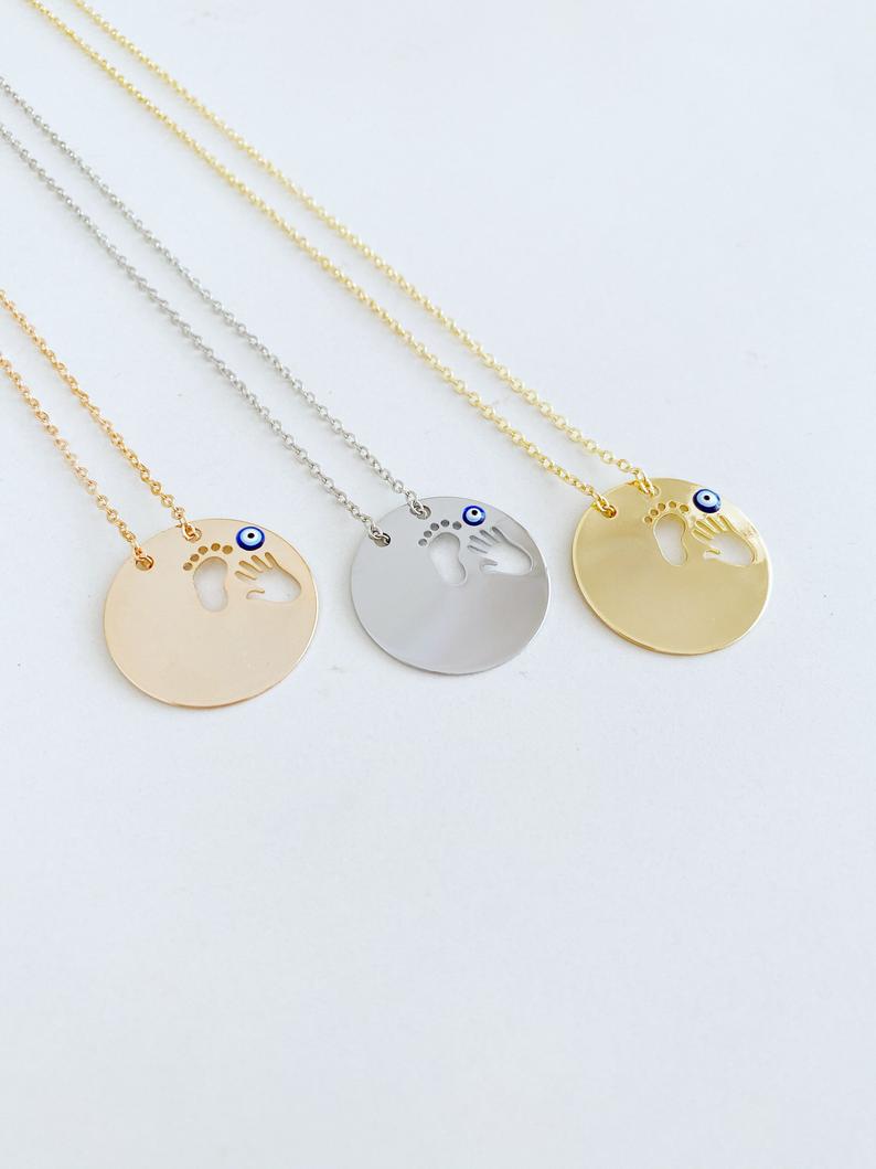 New Baby Necklace featuring an Evil Eye design with baby feet and handprint motifs, available in gold, silver, and rose gold.