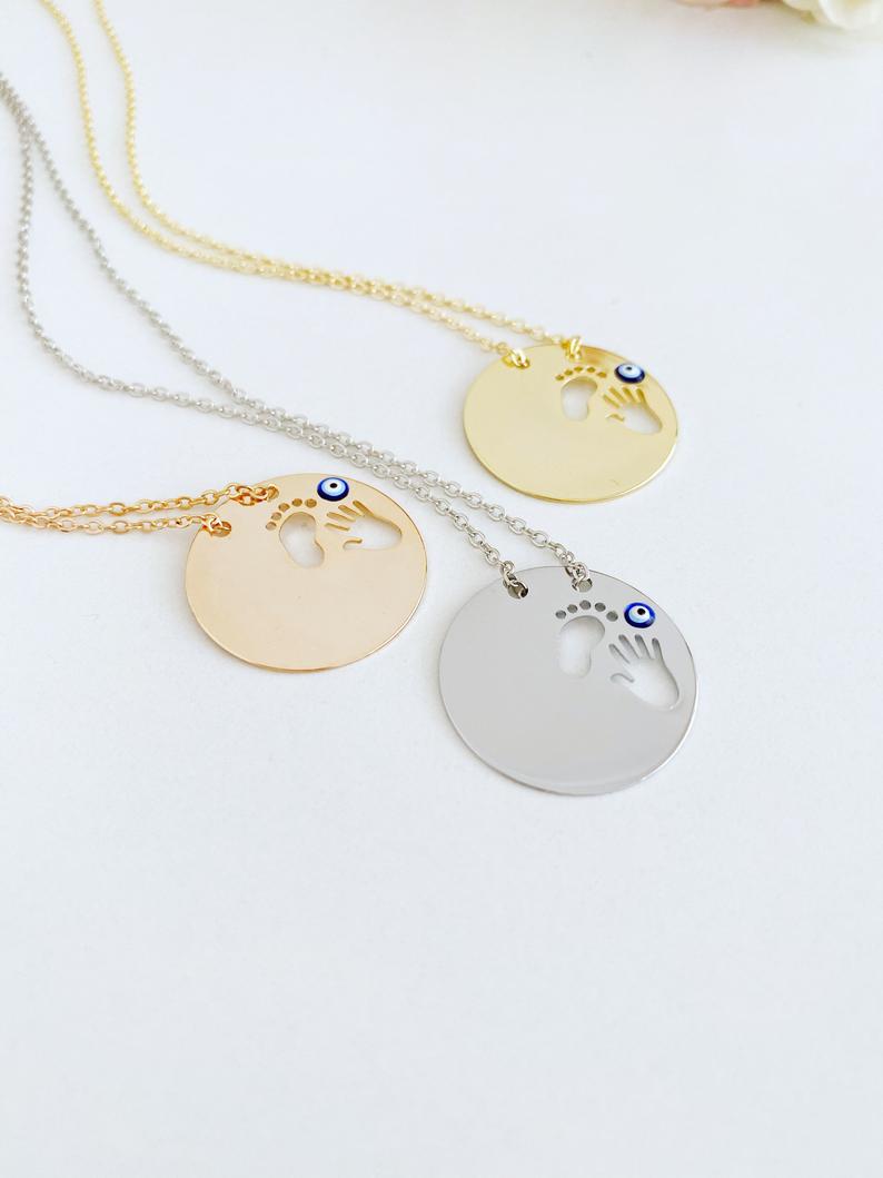 New Baby Necklace featuring an Evil Eye design with baby feet and handprint motifs, available in gold, silver, and rose gold.