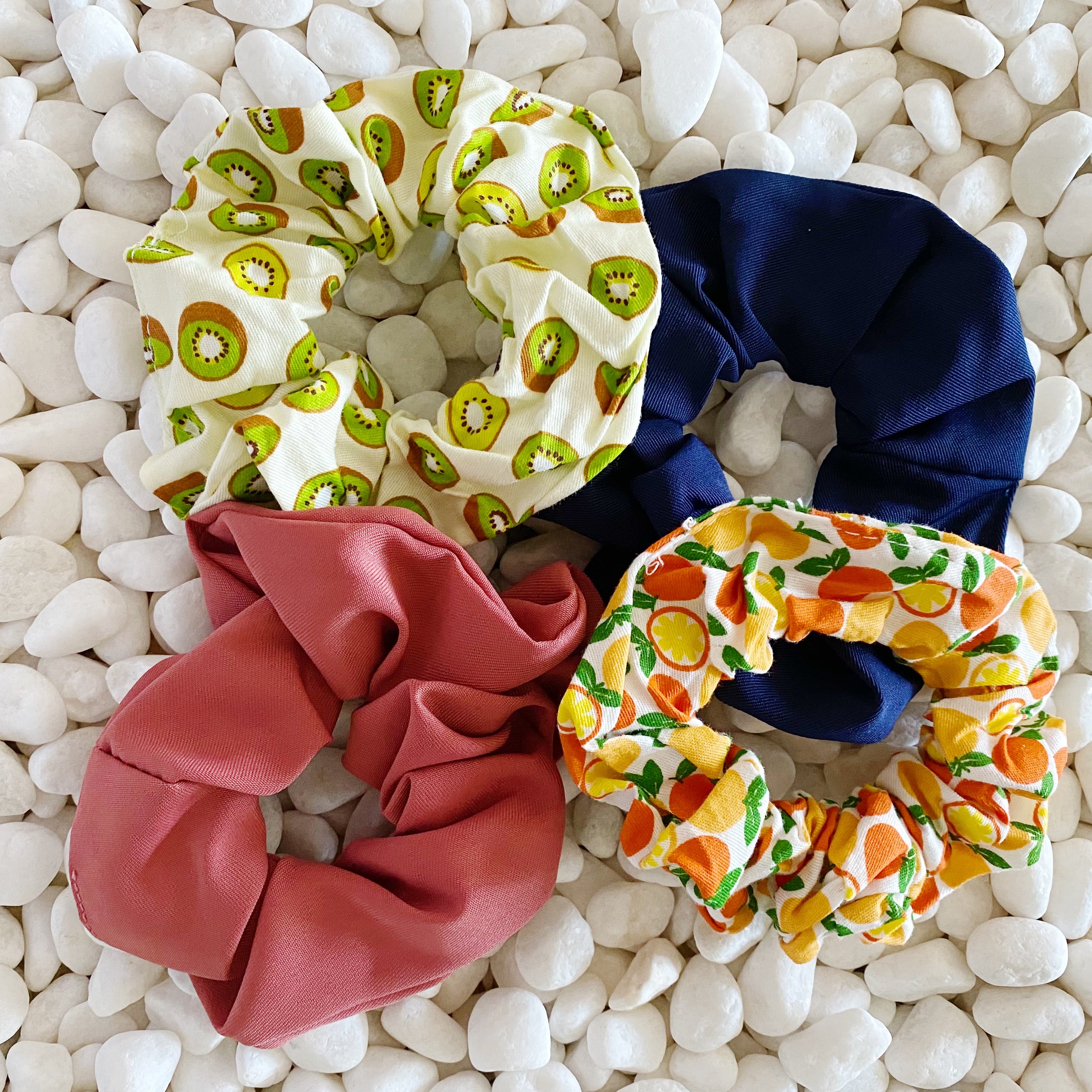 A set of four colorful hair scrunchies featuring two fruit prints and two solid colors, neatly arranged in a clear cello case.