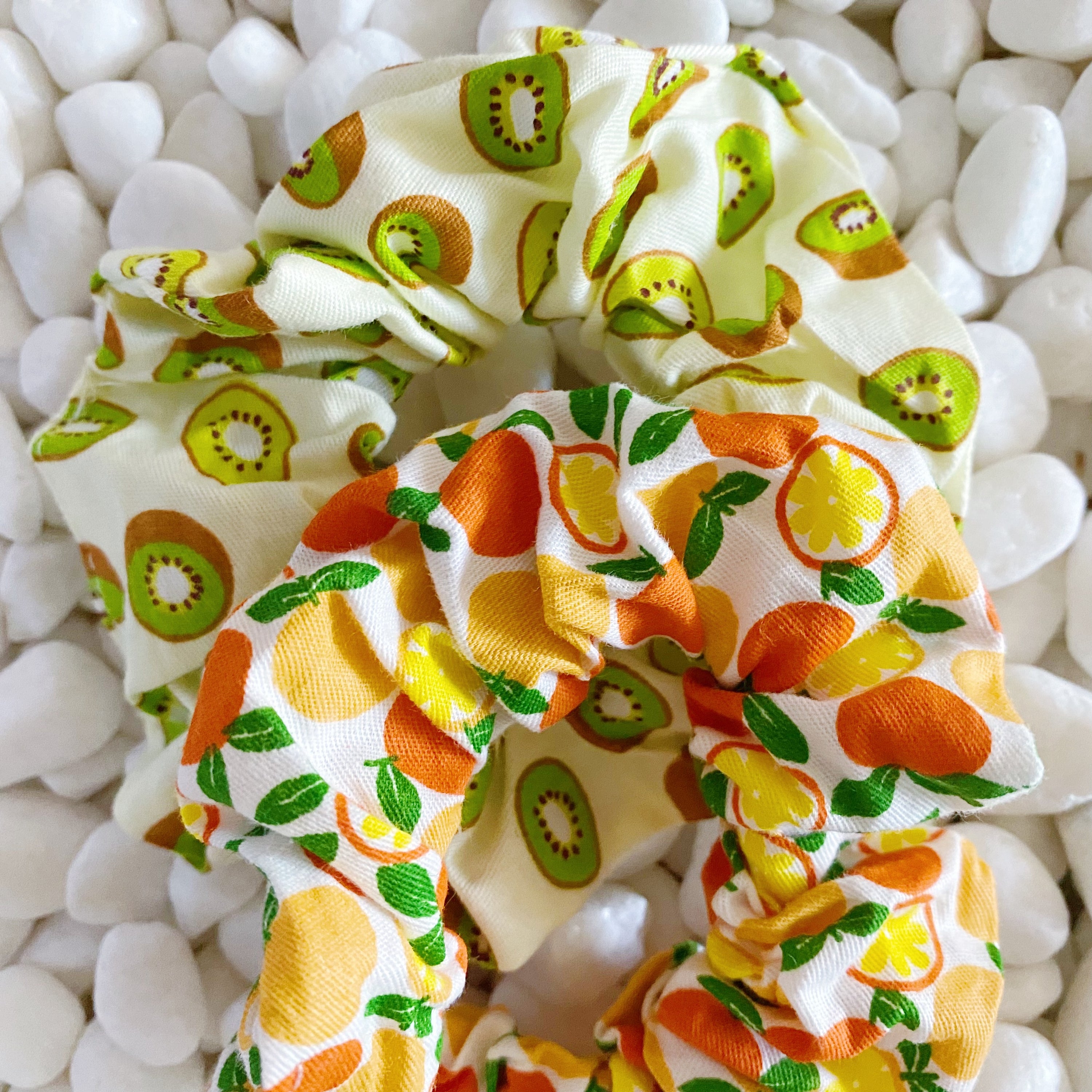 A set of four colorful hair scrunchies featuring two fruit prints and two solid colors, neatly arranged in a clear cello case.