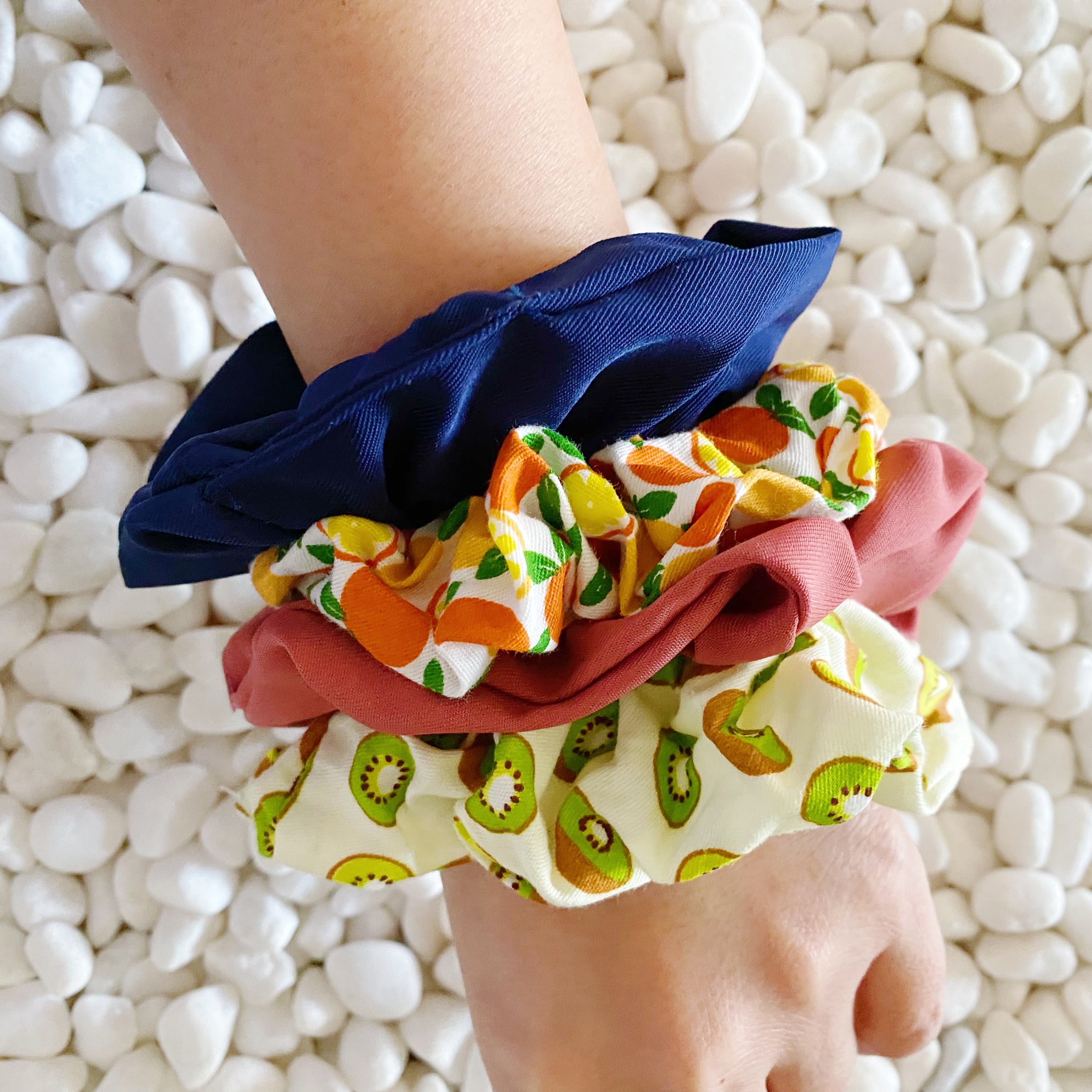 A set of four colorful hair scrunchies featuring two fruit prints and two solid colors, neatly arranged in a clear cello case.