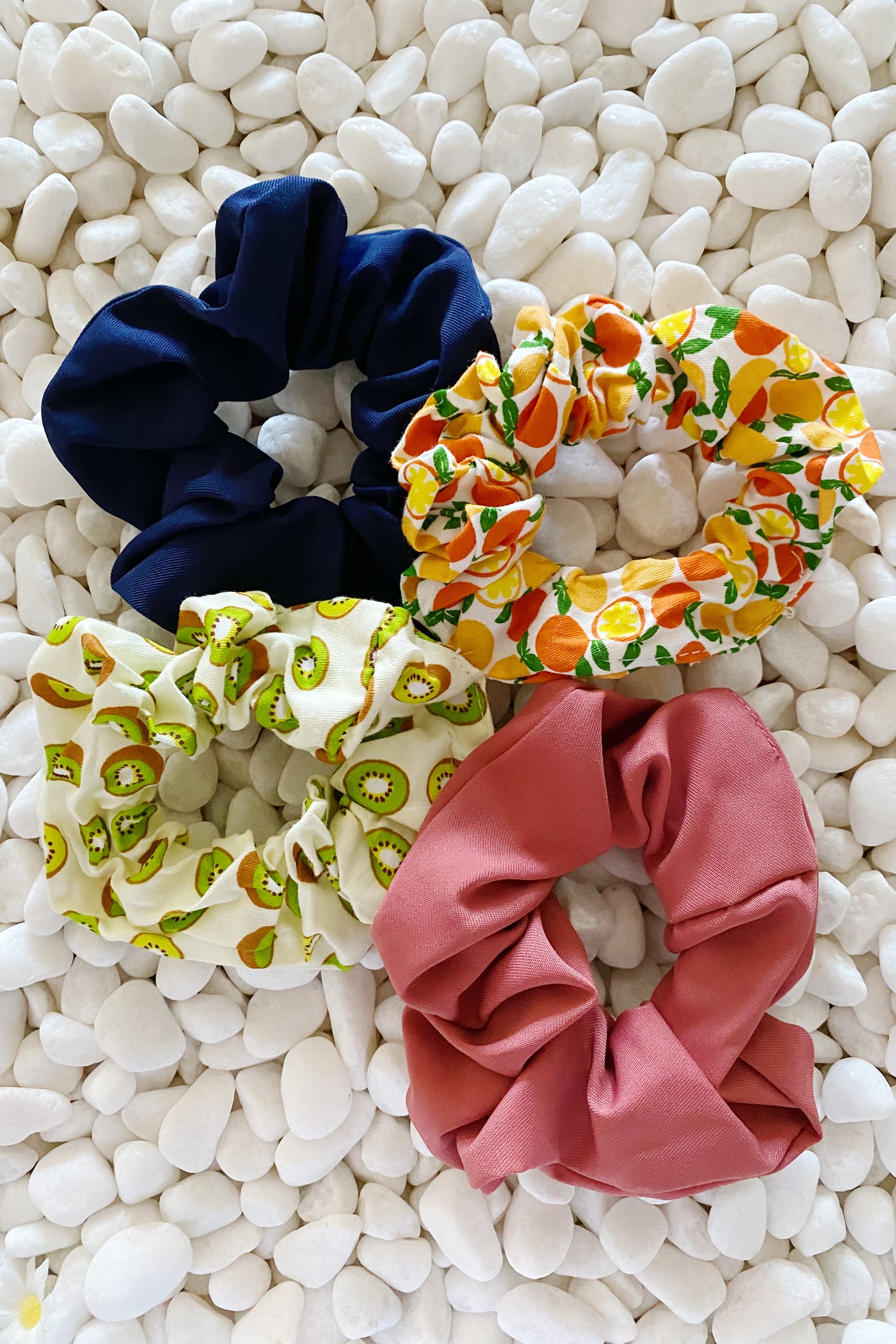 A set of four colorful hair scrunchies featuring two fruit prints and two solid colors, neatly arranged in a clear cello case.