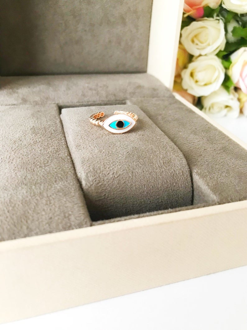 A stylish oval rose gold evil eye ring featuring a white evil eye bead, adjustable design for comfort, and minimalist elegance.