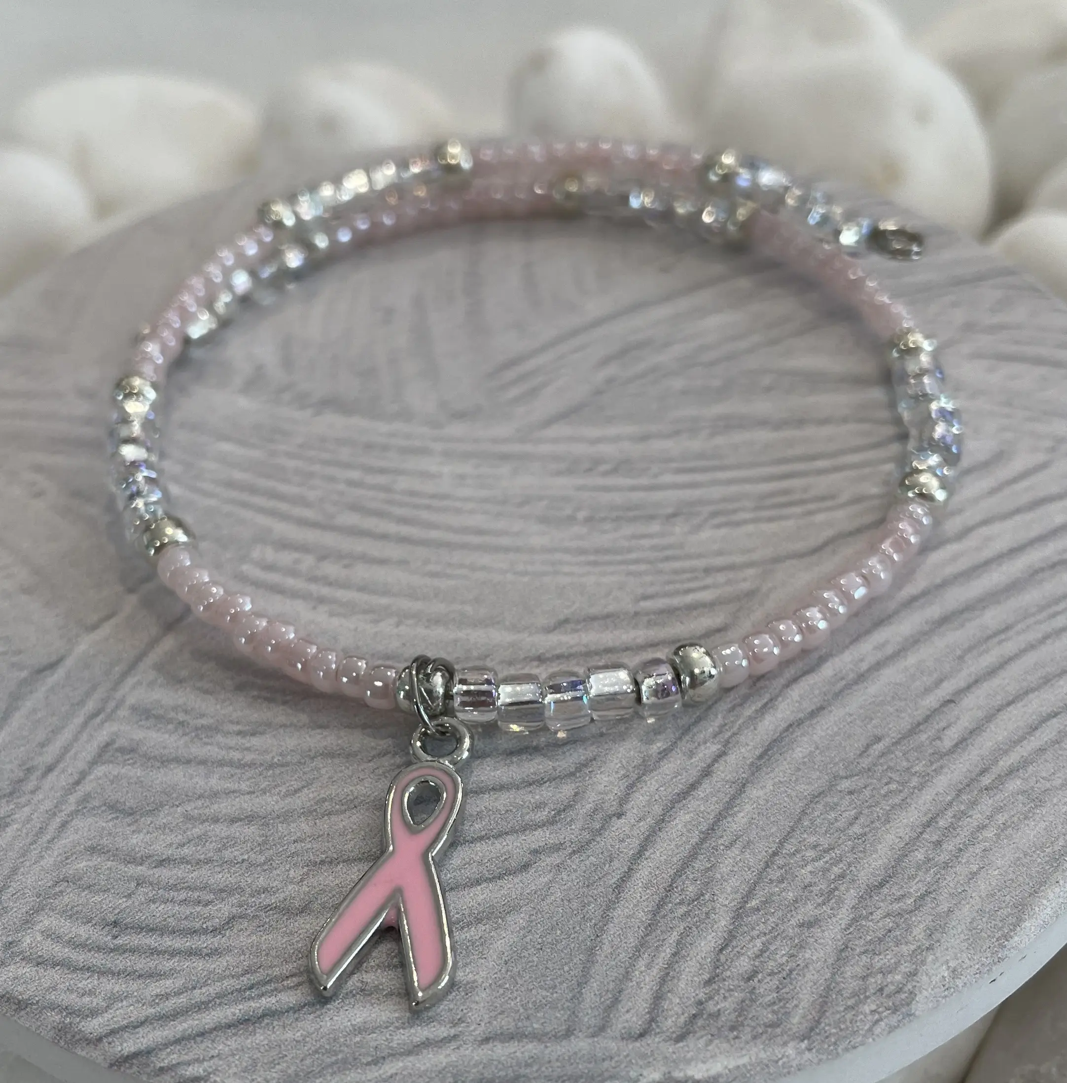 A handmade pale pink charm bracelet featuring glass beads and a Breast Cancer Awareness Ribbon charm, elegantly displayed.