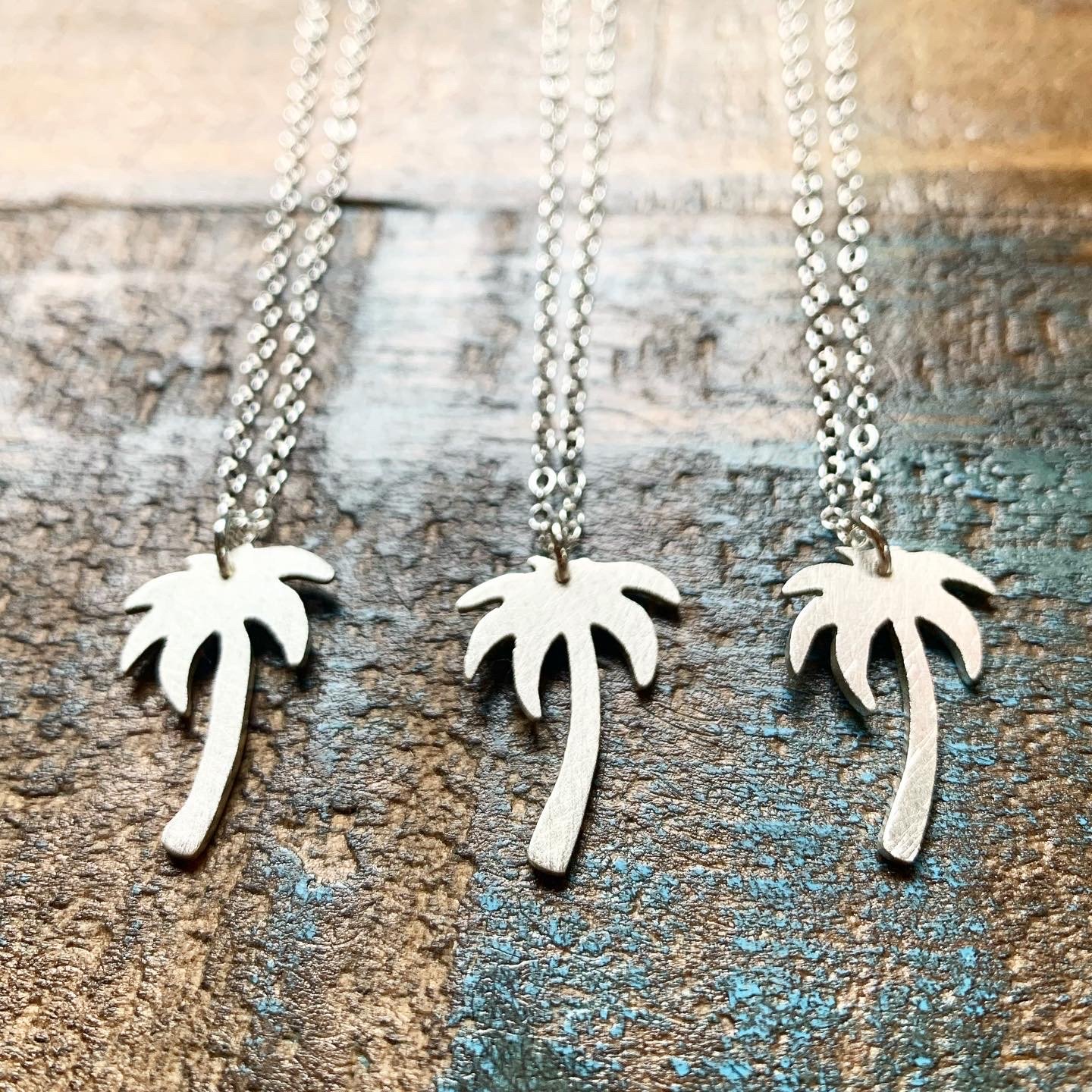 A delicate Palm Tree Charm Necklace featuring a hand-cut palm tree pendant in recycled sterling silver, displayed on a lightweight adjustable chain.