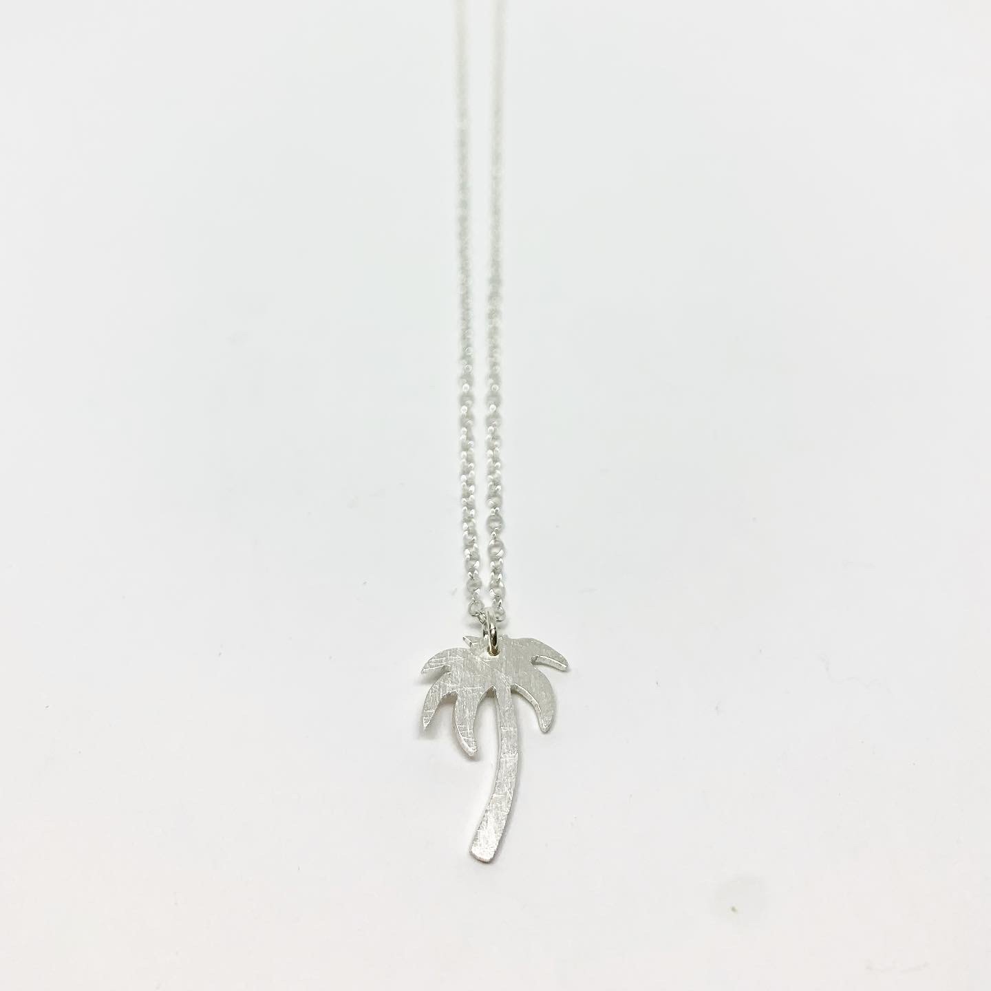 A delicate Palm Tree Charm Necklace featuring a hand-cut palm tree pendant in recycled sterling silver, displayed on a lightweight adjustable chain.