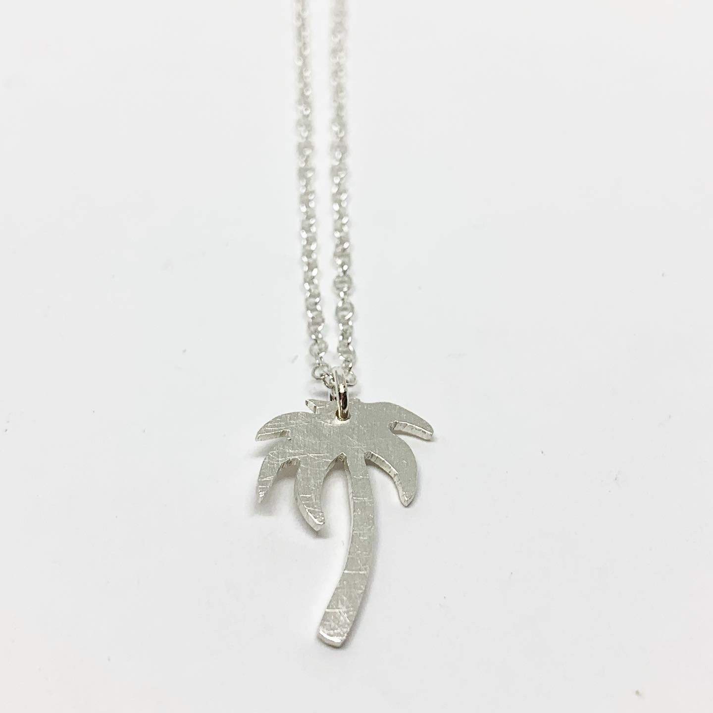 A delicate Palm Tree Charm Necklace featuring a hand-cut palm tree pendant in recycled sterling silver, displayed on a lightweight adjustable chain.