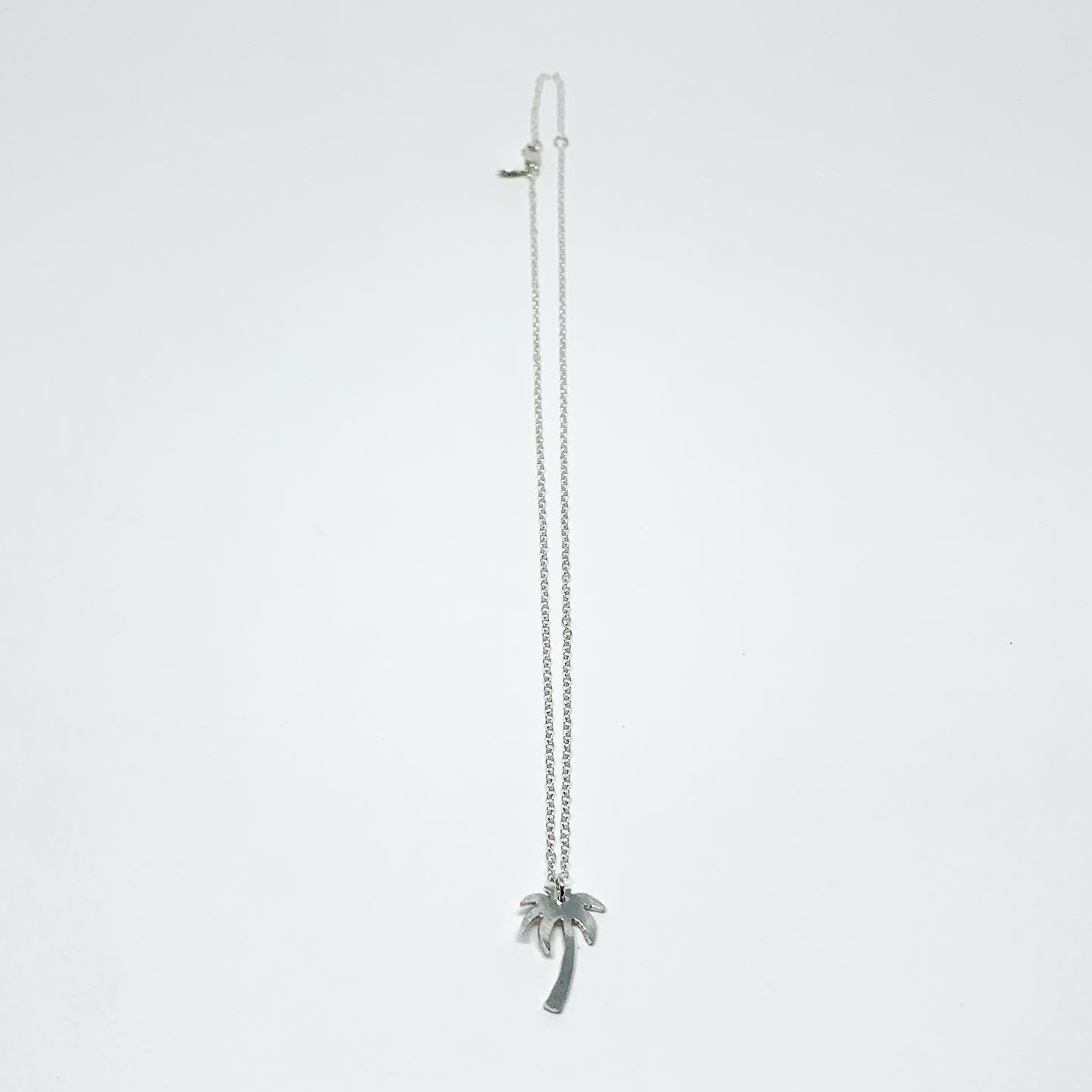 A delicate Palm Tree Charm Necklace featuring a hand-cut palm tree pendant in recycled sterling silver, displayed on a lightweight adjustable chain.