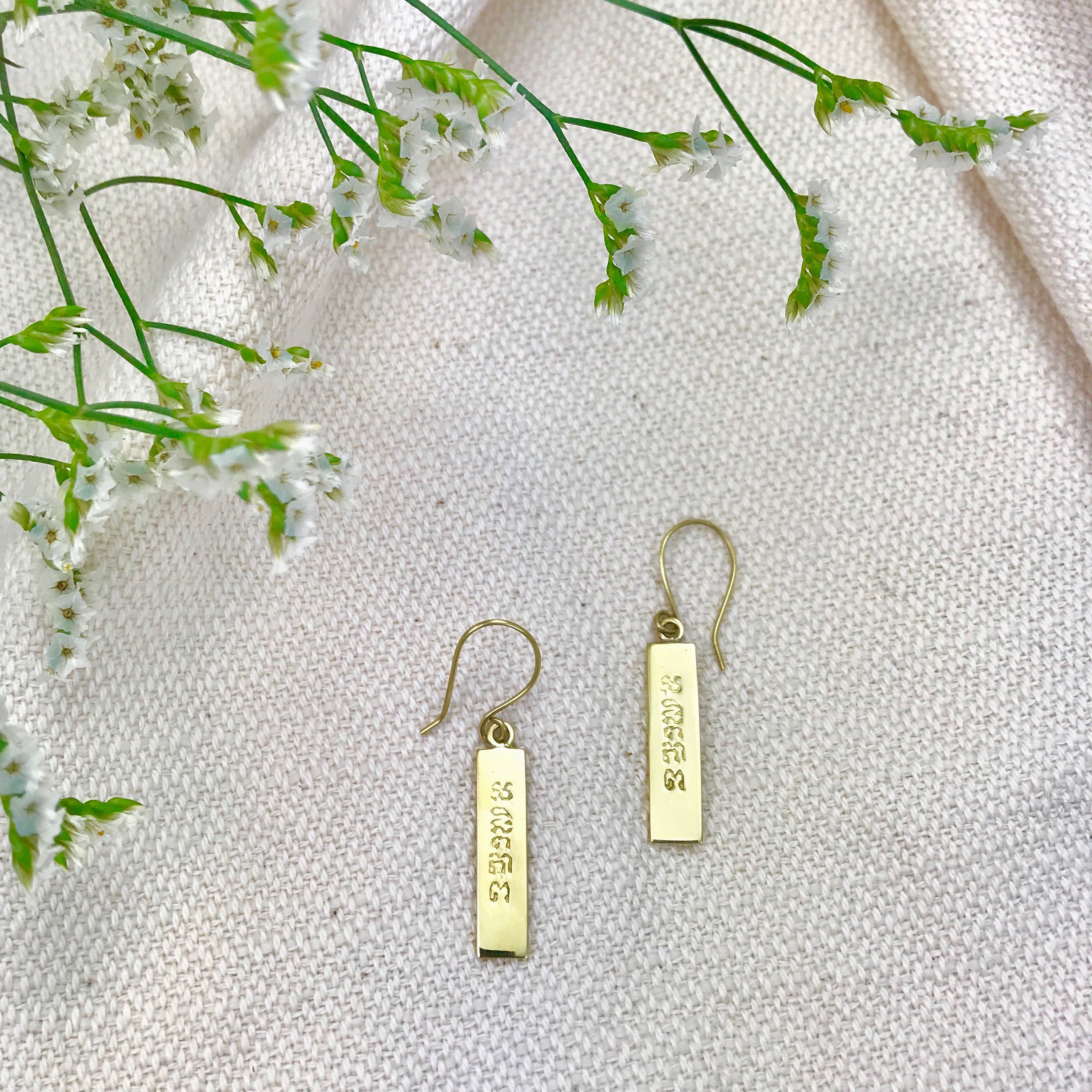 Elegant Peace Bar Earrings handcrafted from recycled brass bombshells, featuring a polished finish and Khmer inscription.