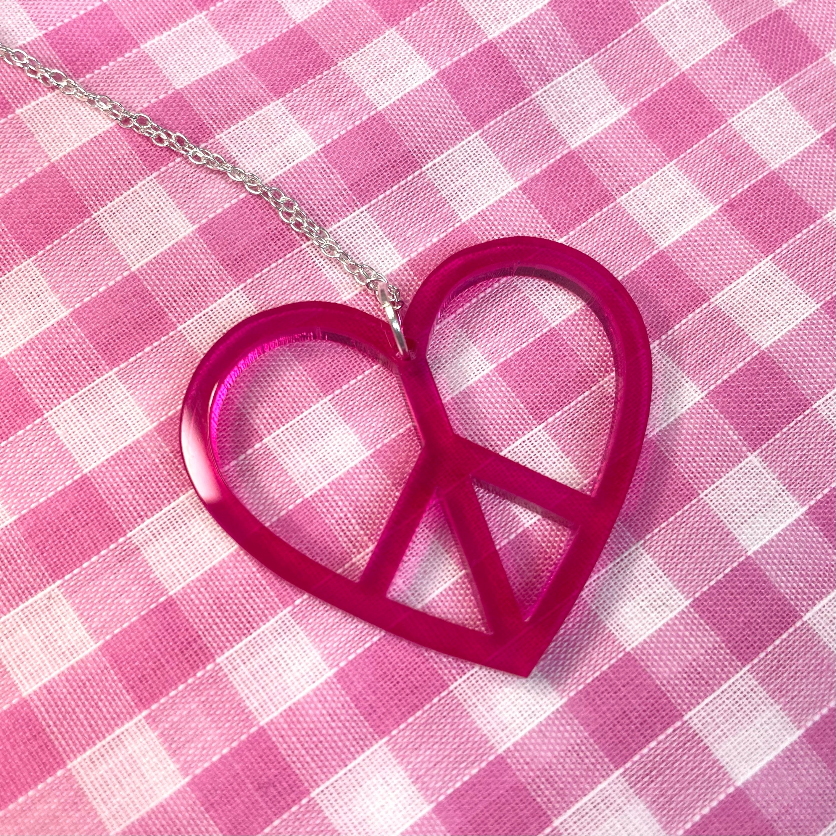 A stylish Peace Heart Necklace featuring a laser-cut acrylic heart on a sterling silver chain, inspired by 1960s and 70s fashion.