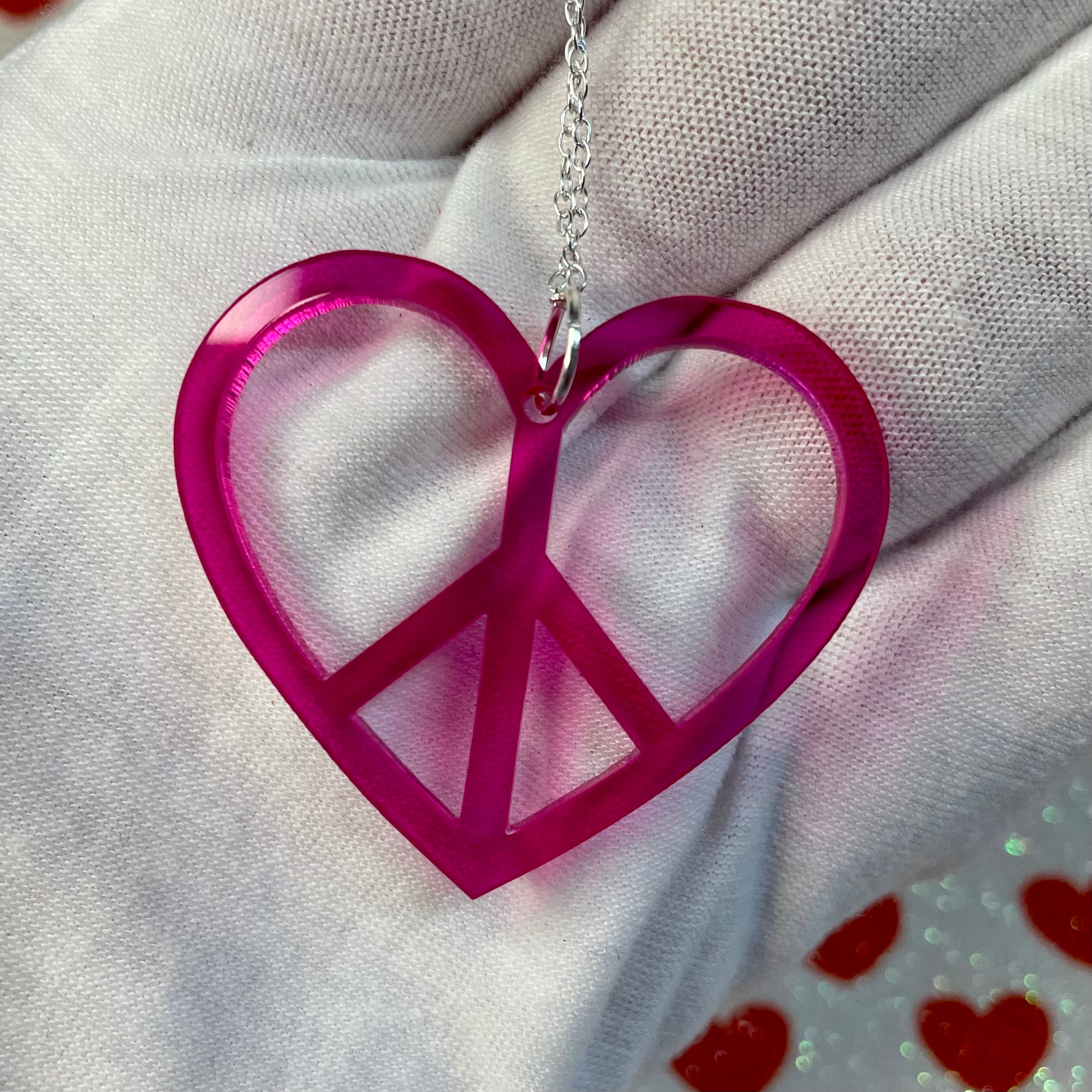 A stylish Peace Heart Necklace featuring a laser-cut acrylic heart on a sterling silver chain, inspired by 1960s and 70s fashion.