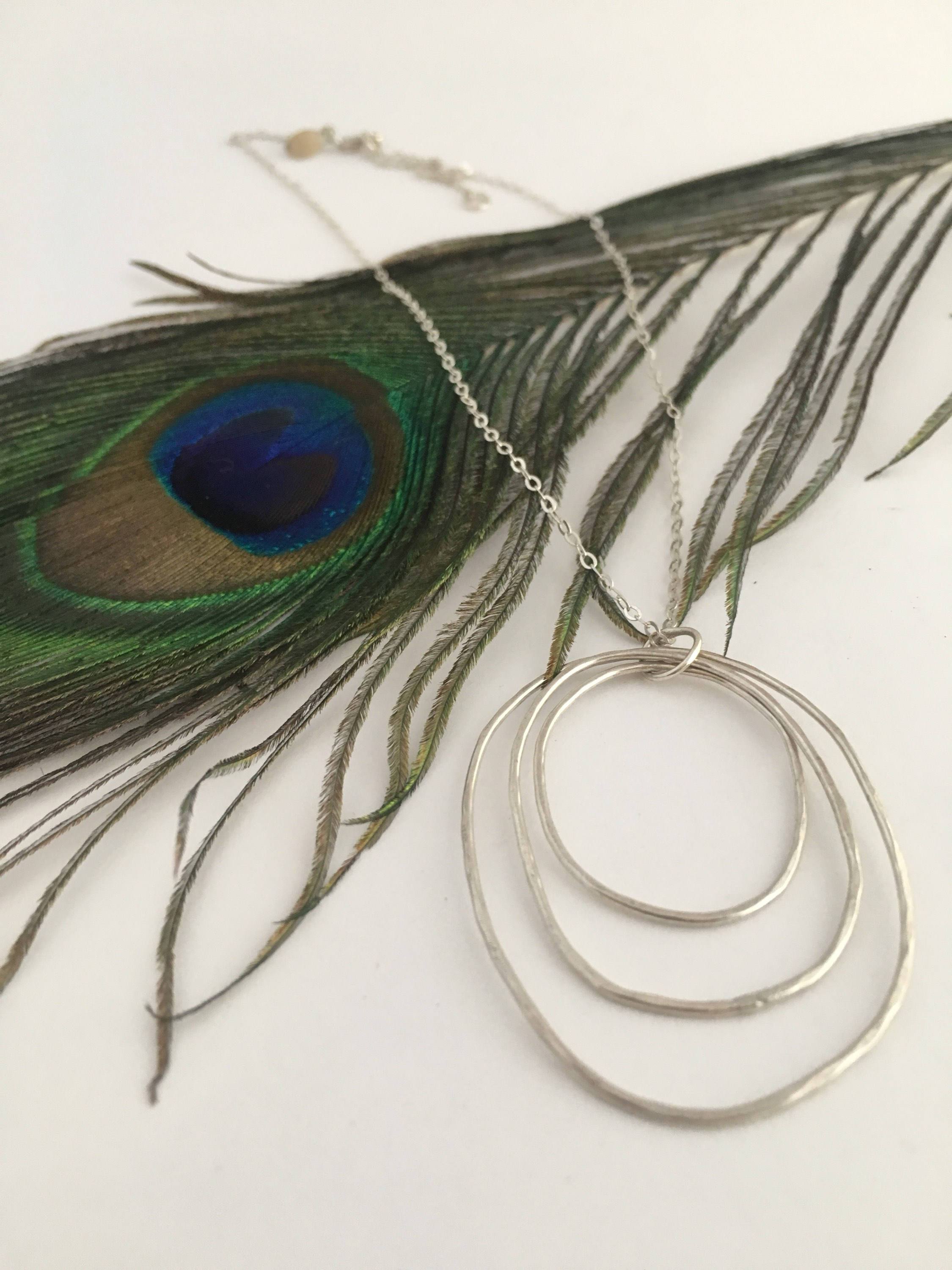 A beautifully handcrafted Peacock Feather Necklace made from recycled metals, showcasing intricate feather patterns.