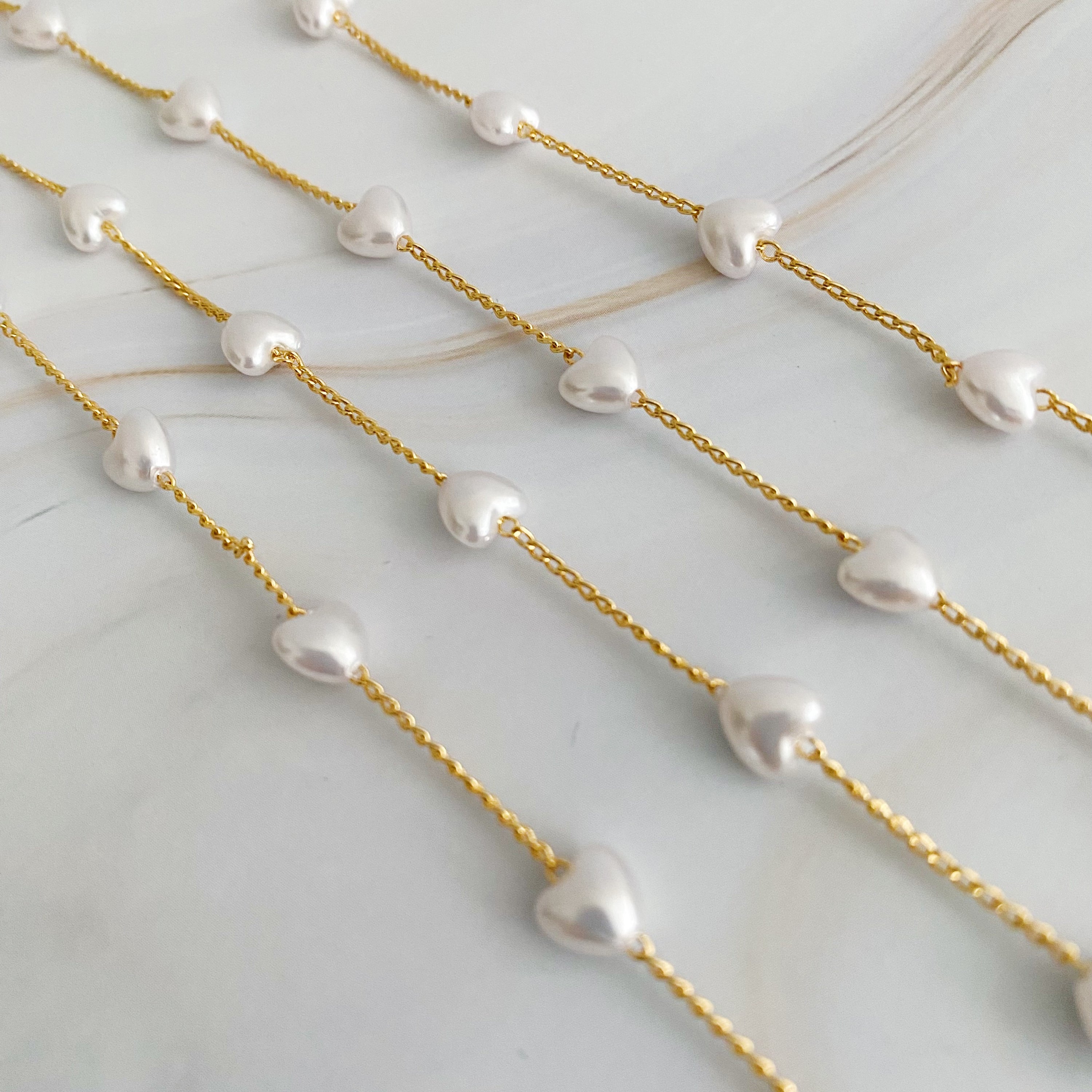 A beautiful Pearl Heart Long Chain Necklace featuring creamy pearl hearts on a 34-inch gold plated chain.