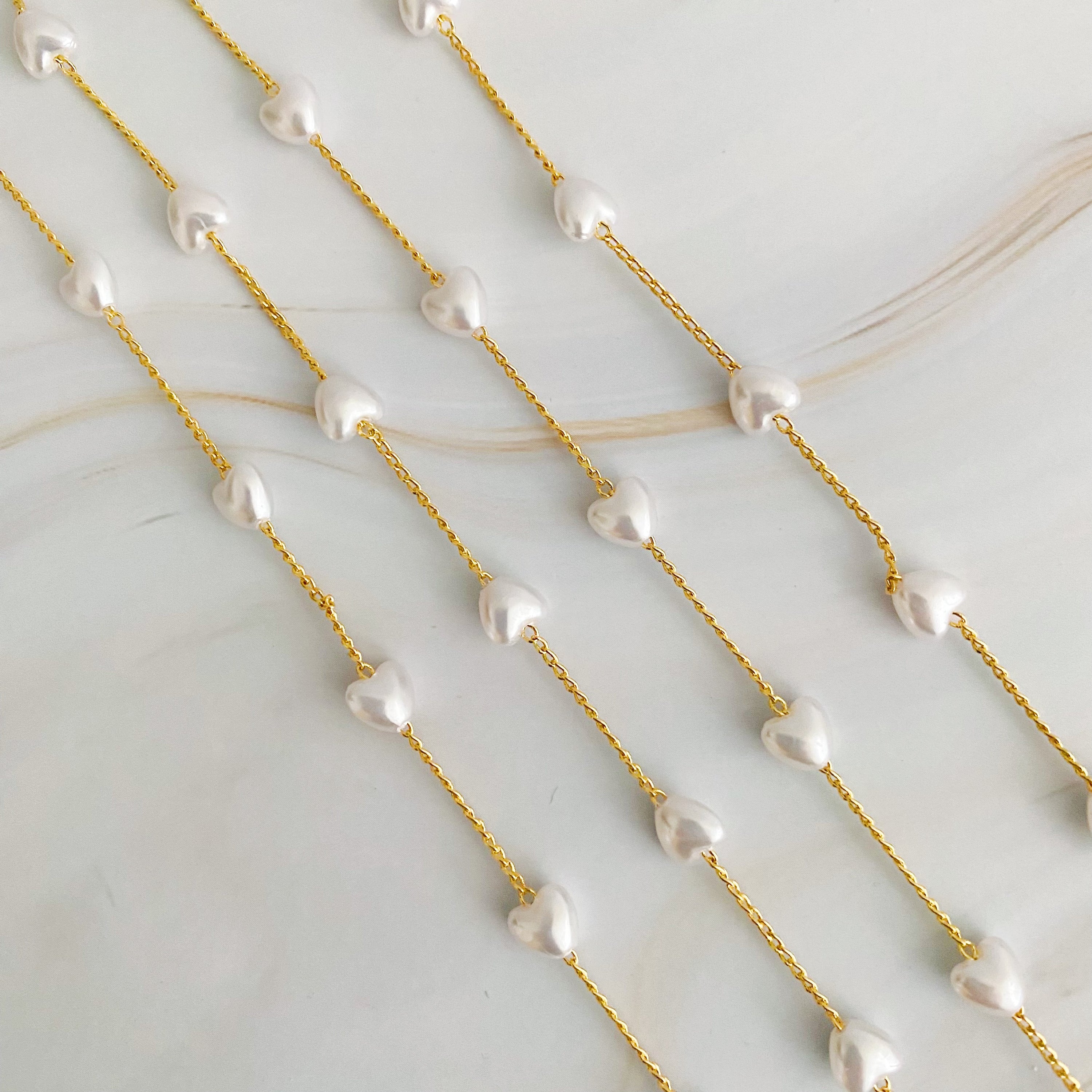 A beautiful Pearl Heart Long Chain Necklace featuring creamy pearl hearts on a 34-inch gold plated chain.