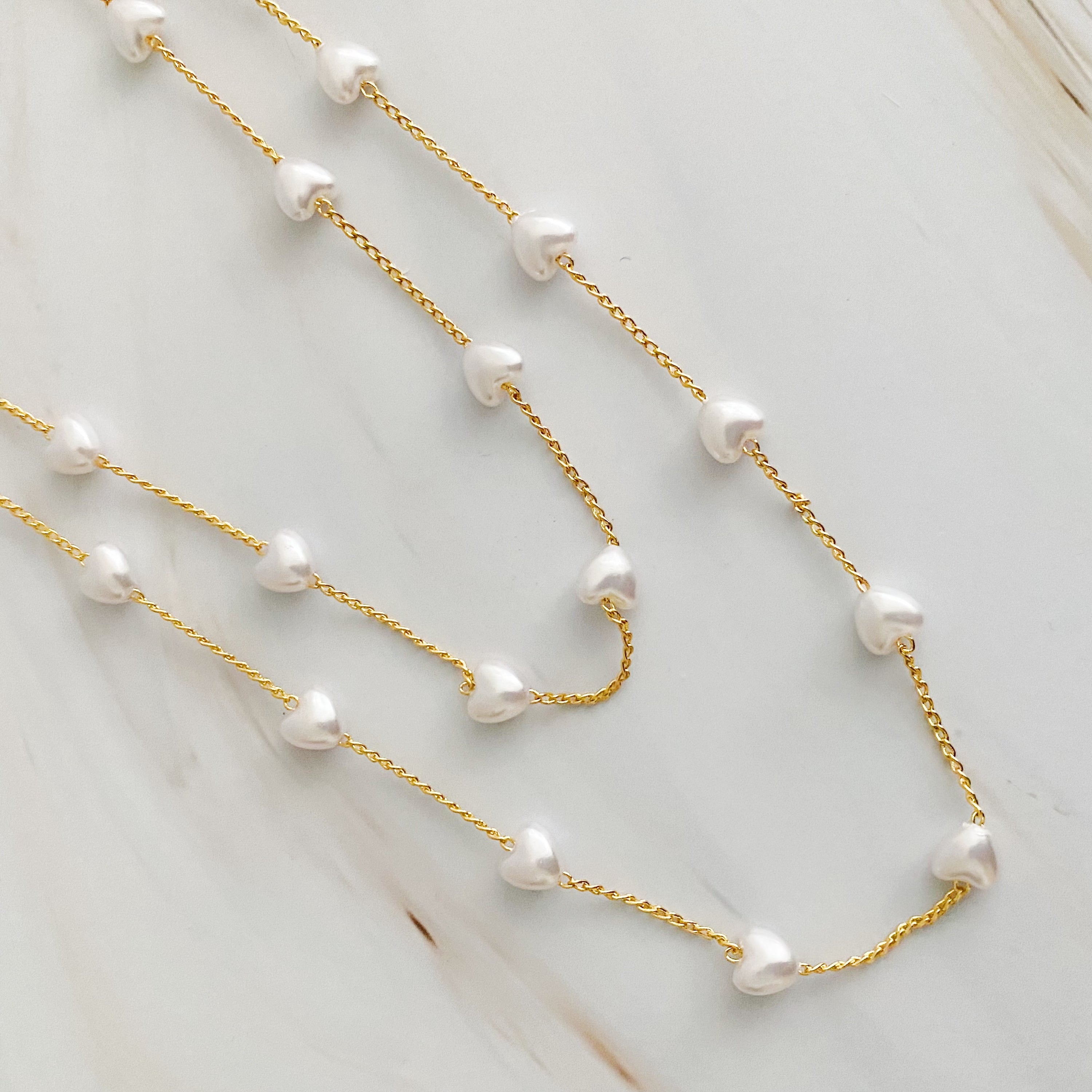 A beautiful Pearl Heart Long Chain Necklace featuring creamy pearl hearts on a 34-inch gold plated chain.