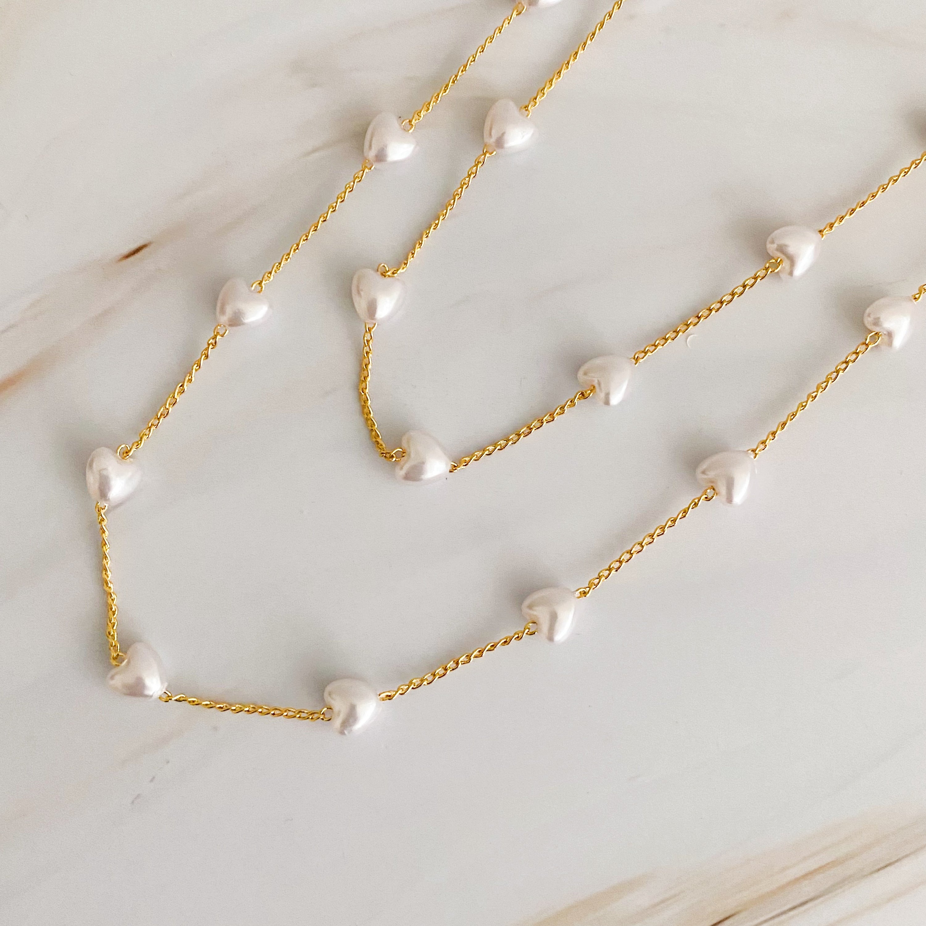 A beautiful Pearl Heart Long Chain Necklace featuring creamy pearl hearts on a 34-inch gold plated chain.